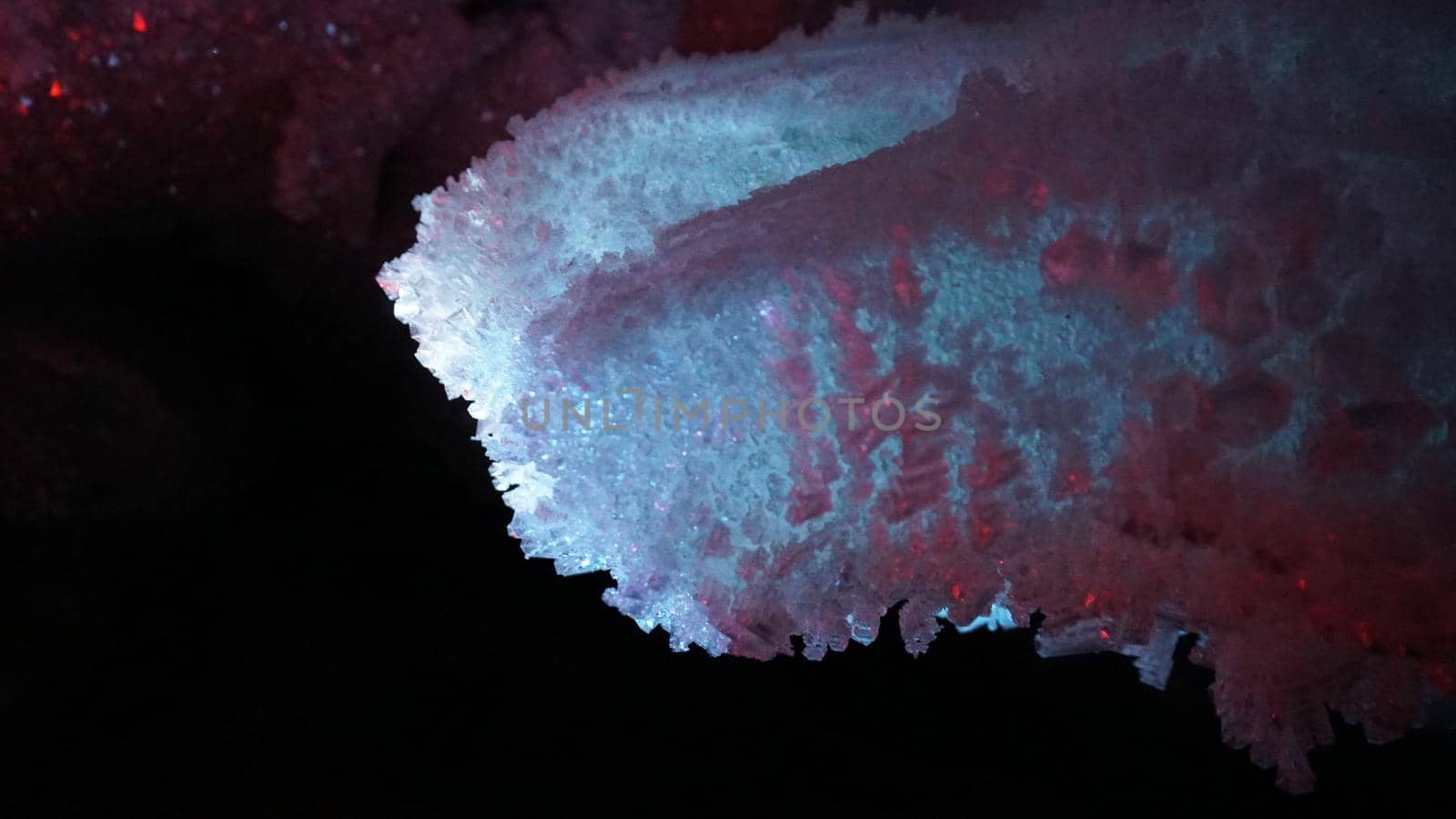 Macro photography of ice growths in a cave. Snow and ice of interesting shapes grow on the walls of the cave. Stalactites hang. Huge ice walls shimmer from the light of the lantern. Almaty, Kazakhstan