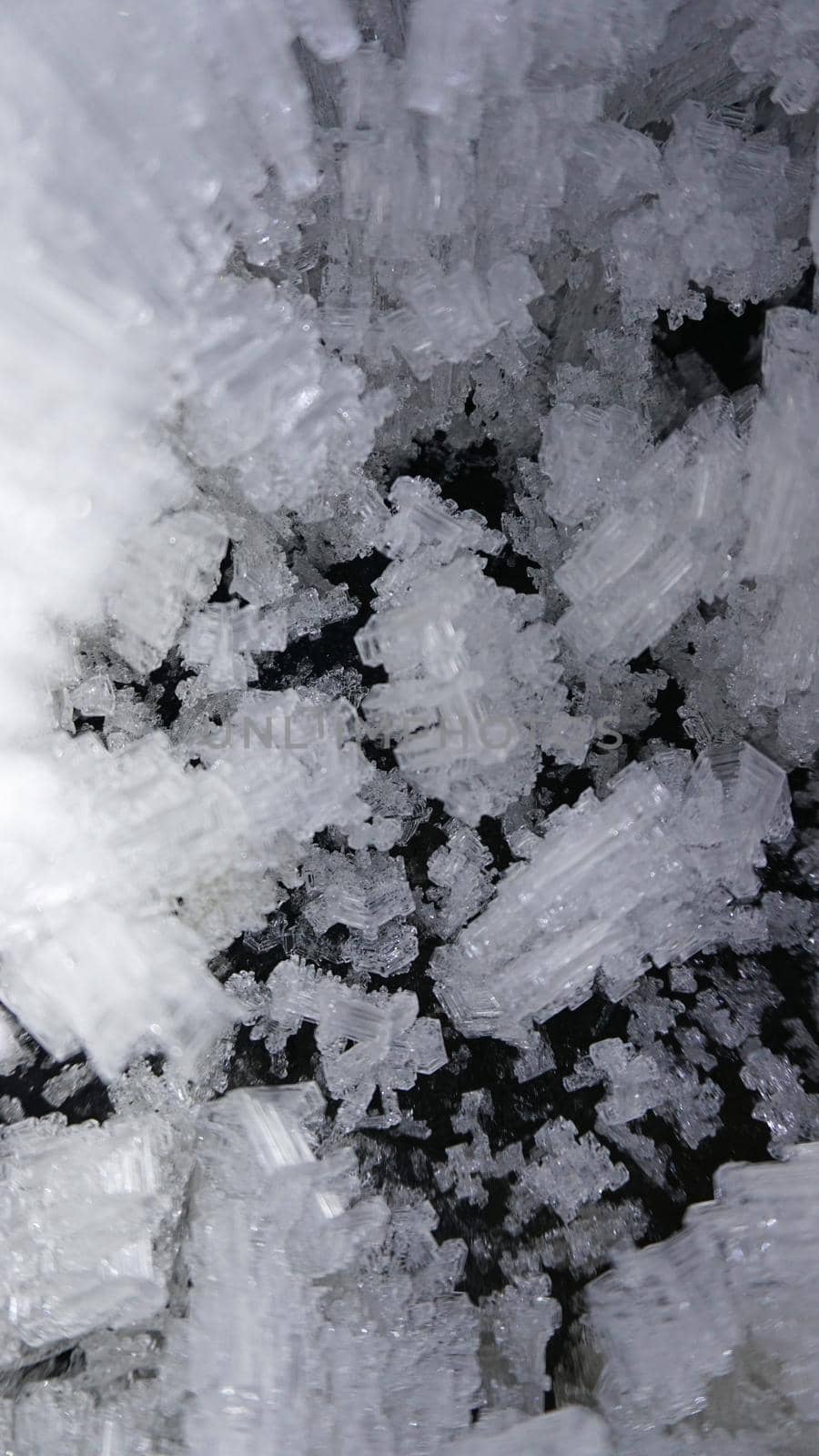 Macro photography of ice growths in a cave. Snow and ice of interesting shapes grow on the walls of the cave. Stalactites hang. Huge ice walls shimmer from the light of the lantern. Almaty, Kazakhstan