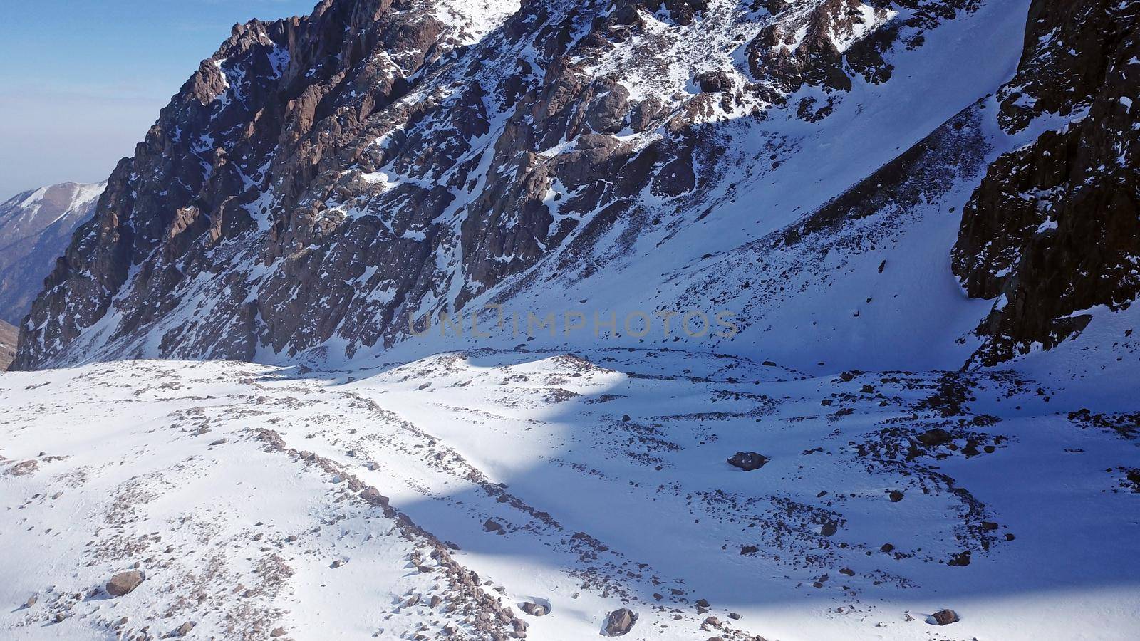 High snow-capped peaks and glaciers. Top view from the drone. Steep cliffs, the wind blows away the snow. There is a lone nunatak. Moraine frozen lake. Climb to the peak. Bogdanovich Glacier, Almaty