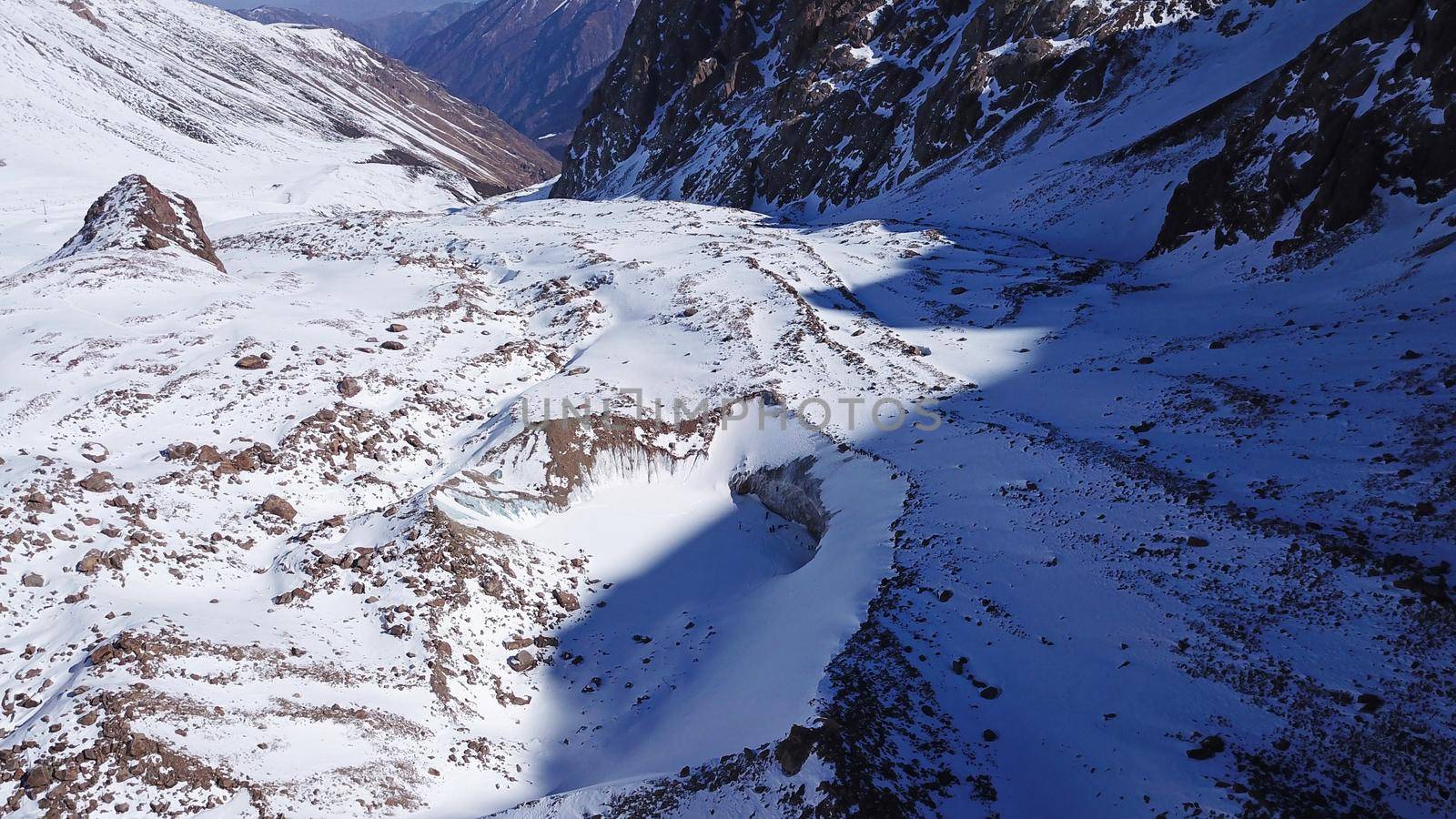 High snow-capped peaks and glaciers. Top view from the drone. Steep cliffs, the wind blows away the snow. There is a lone nunatak. Moraine frozen lake. Climb to the peak. Bogdanovich Glacier, Almaty