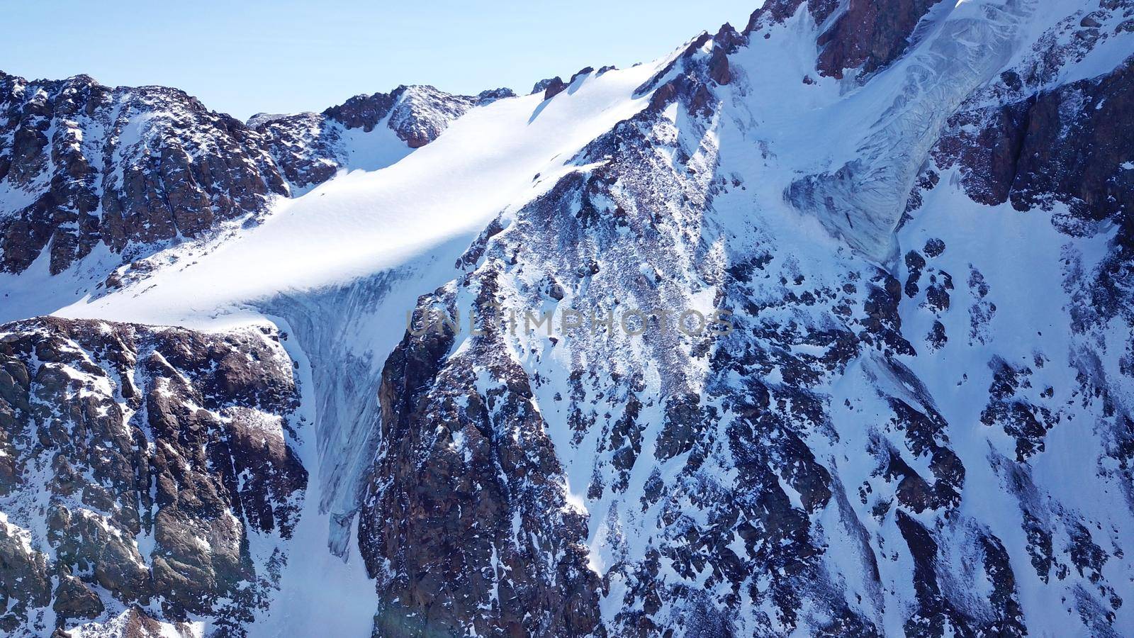 High snow-capped peaks and glaciers. Top view from the drone. Steep cliffs, the wind blows away the snow. There is a lone nunatak. Moraine frozen lake. Climb to the peak. Bogdanovich Glacier, Almaty