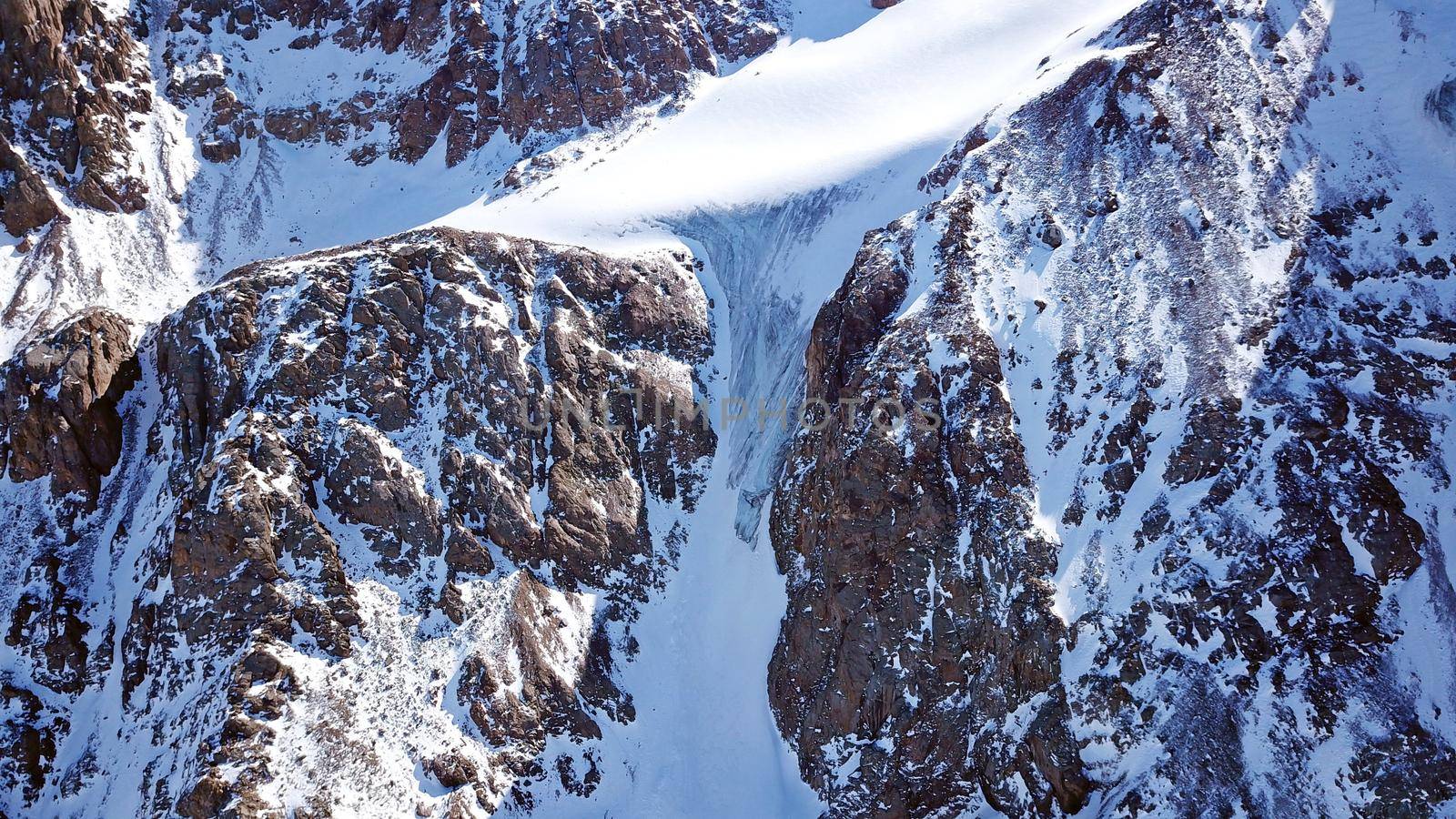 High snow-capped peaks and glaciers. Top view from the drone. Steep cliffs, the wind blows away the snow. There is a lone nunatak. Moraine frozen lake. Climb to the peak. Bogdanovich Glacier, Almaty