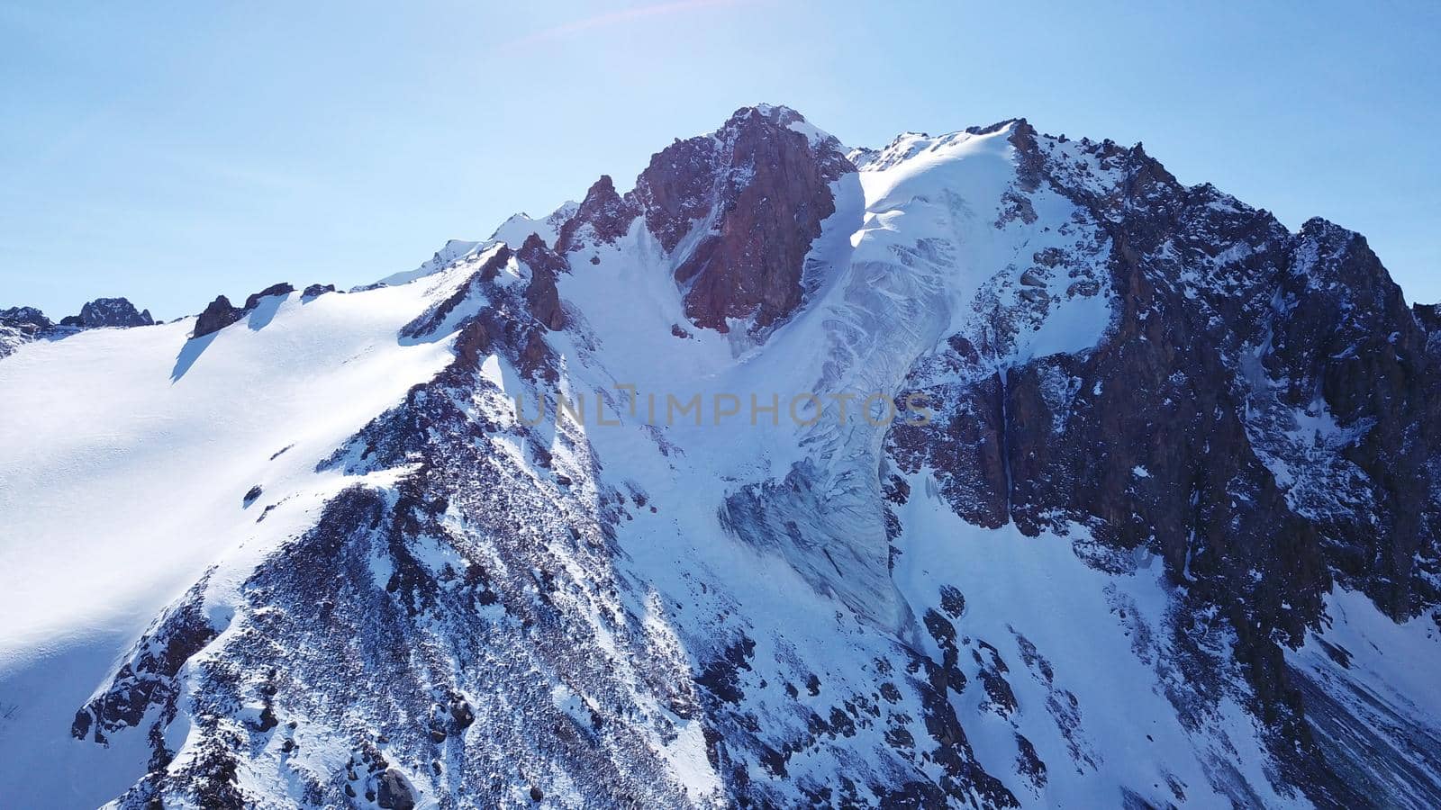 High snow-capped peaks and glaciers. Top view from the drone. Steep cliffs, the wind blows away the snow. There is a lone nunatak. Moraine frozen lake. Climb to the peak. Bogdanovich Glacier, Almaty