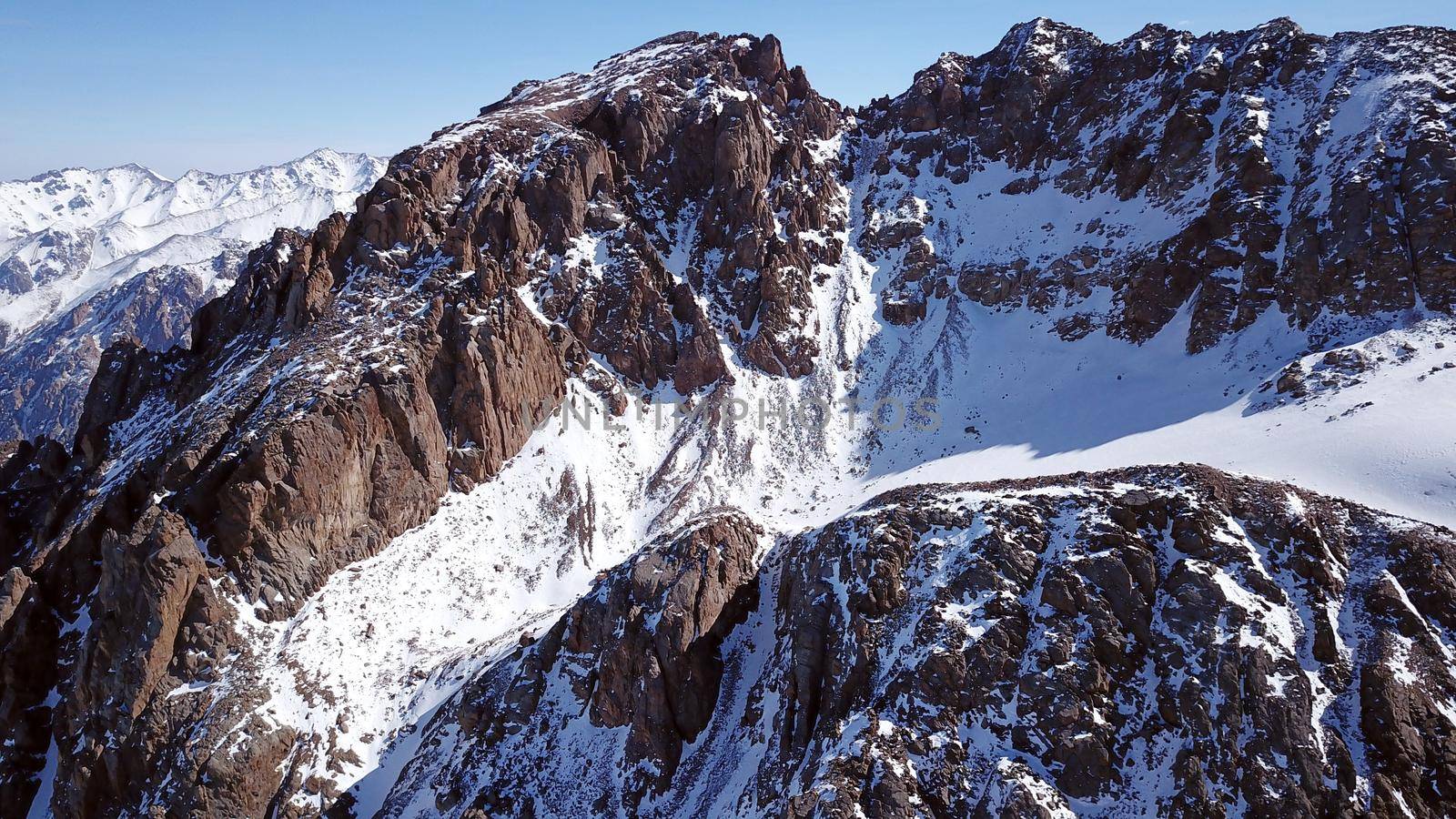 High snow-capped peaks and glaciers. Top view from the drone. Steep cliffs, the wind blows away the snow. There is a lone nunatak. Moraine frozen lake. Climb to the peak. Bogdanovich Glacier, Almaty