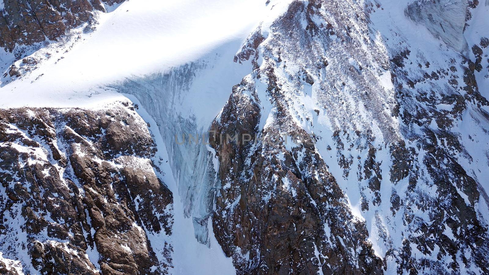 High snow-capped peaks and glaciers. Top view from the drone. Steep cliffs, the wind blows away the snow. There is a lone nunatak. Moraine frozen lake. Climb to the peak. Bogdanovich Glacier, Almaty