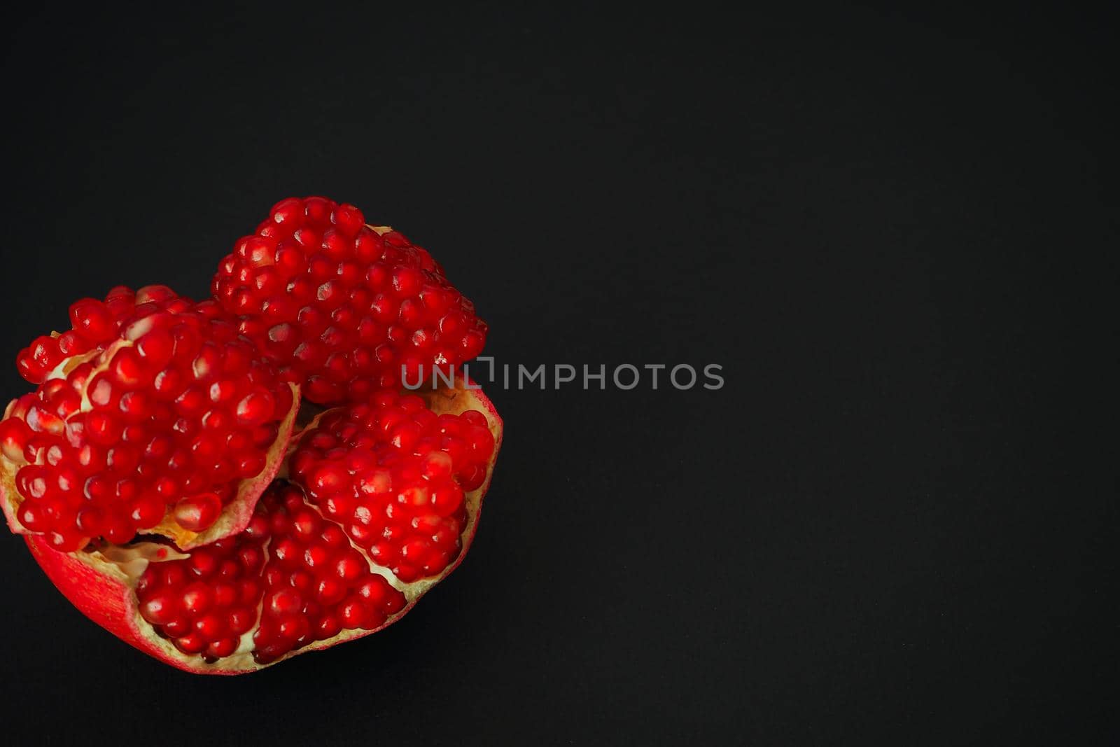 The fruit of a ripe pomegranate. Red fruit with juicy grains. Isolated on a black background. Close-up.