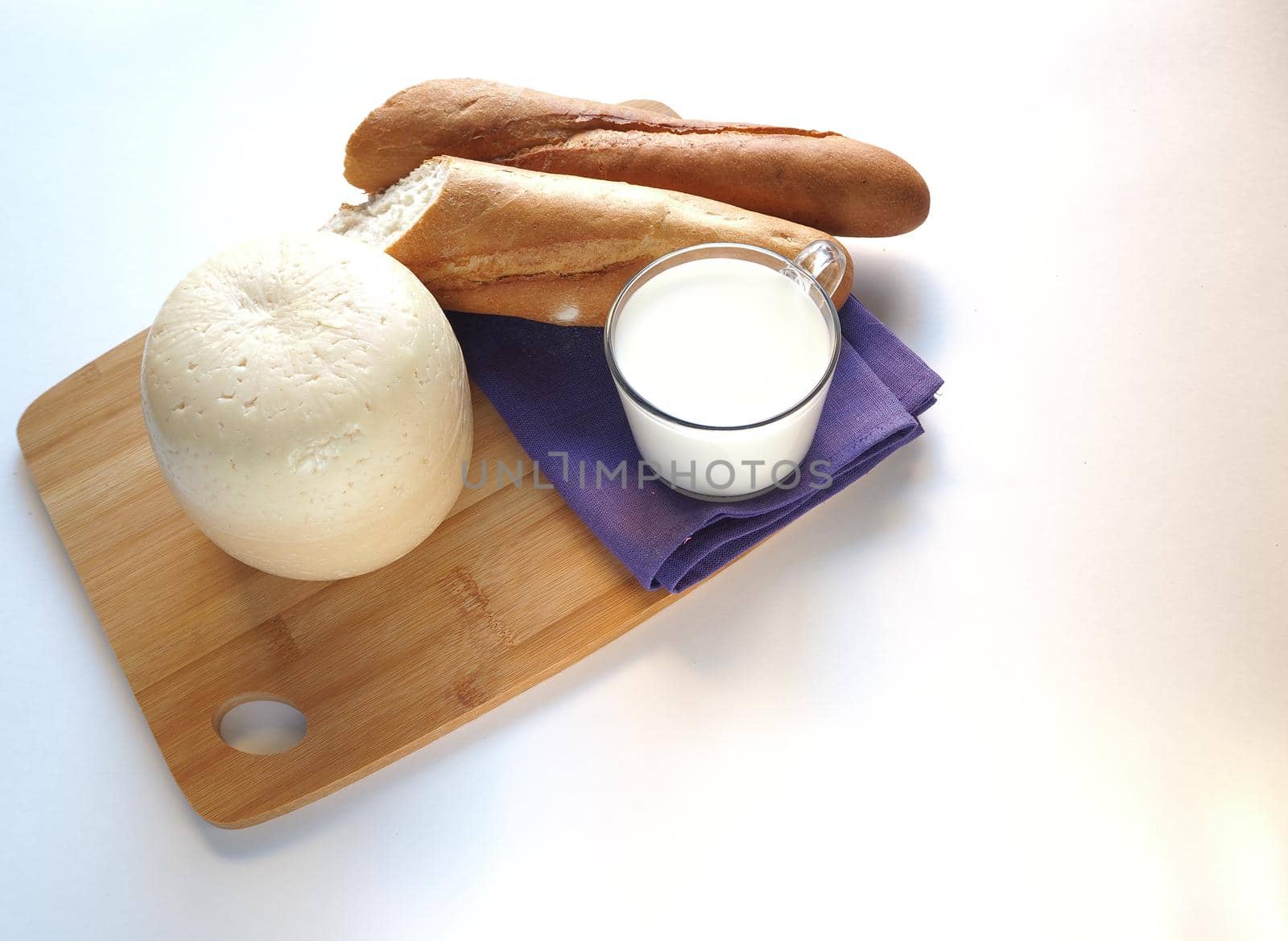 Round head of cheese with bread and milk on a wooden tray. 