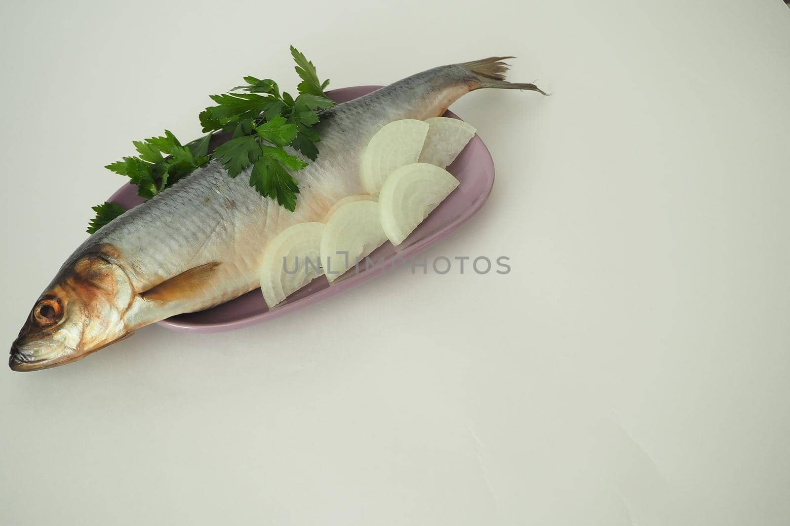 Fish. It's a whole herring. Undivided herring with onions and parsley. Close-up, white background.