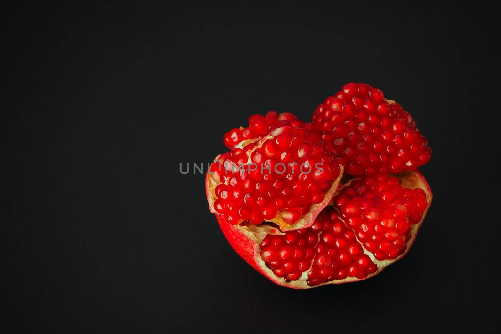 The fruit of a ripe pomegranate. Red fruit with juicy grains. Isolated on a black background. Close-up.