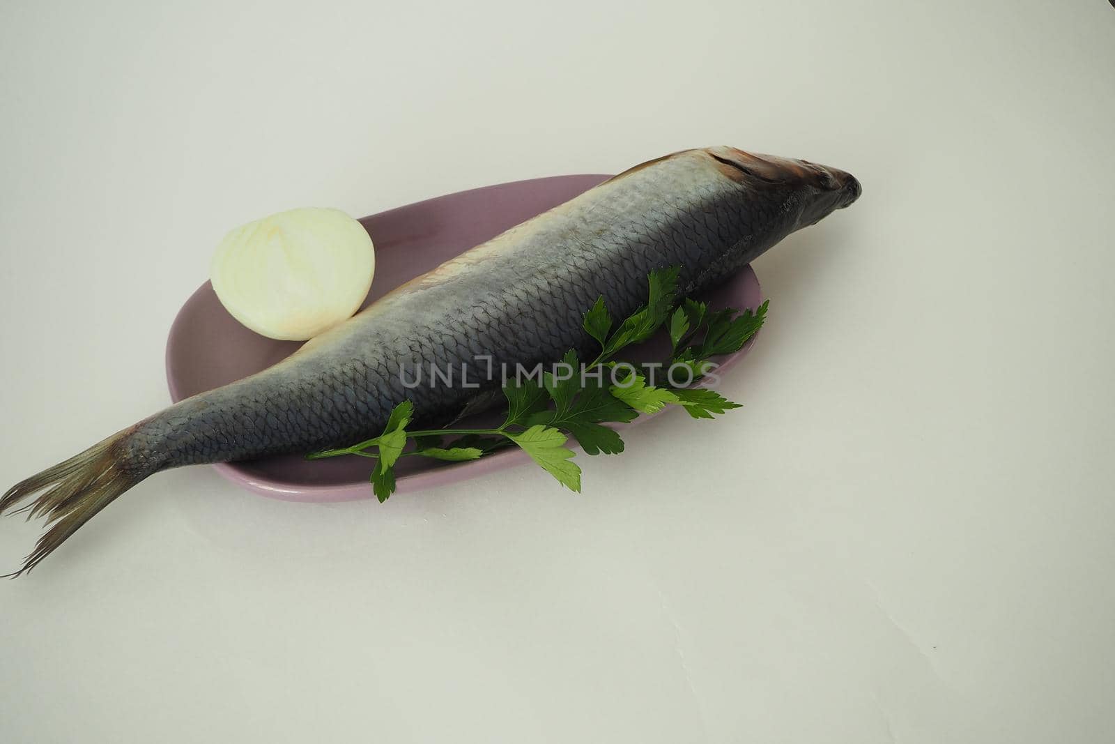 Fish. It's a whole herring. Undivided herring with onions and parsley. Close-up, white background.