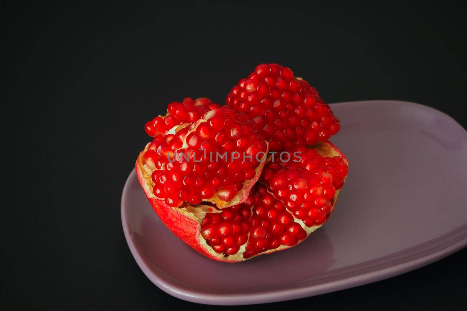 The fruit of a ripe pomegranate. Red fruit with juicy grains. Isolated on a black background. Close-up.