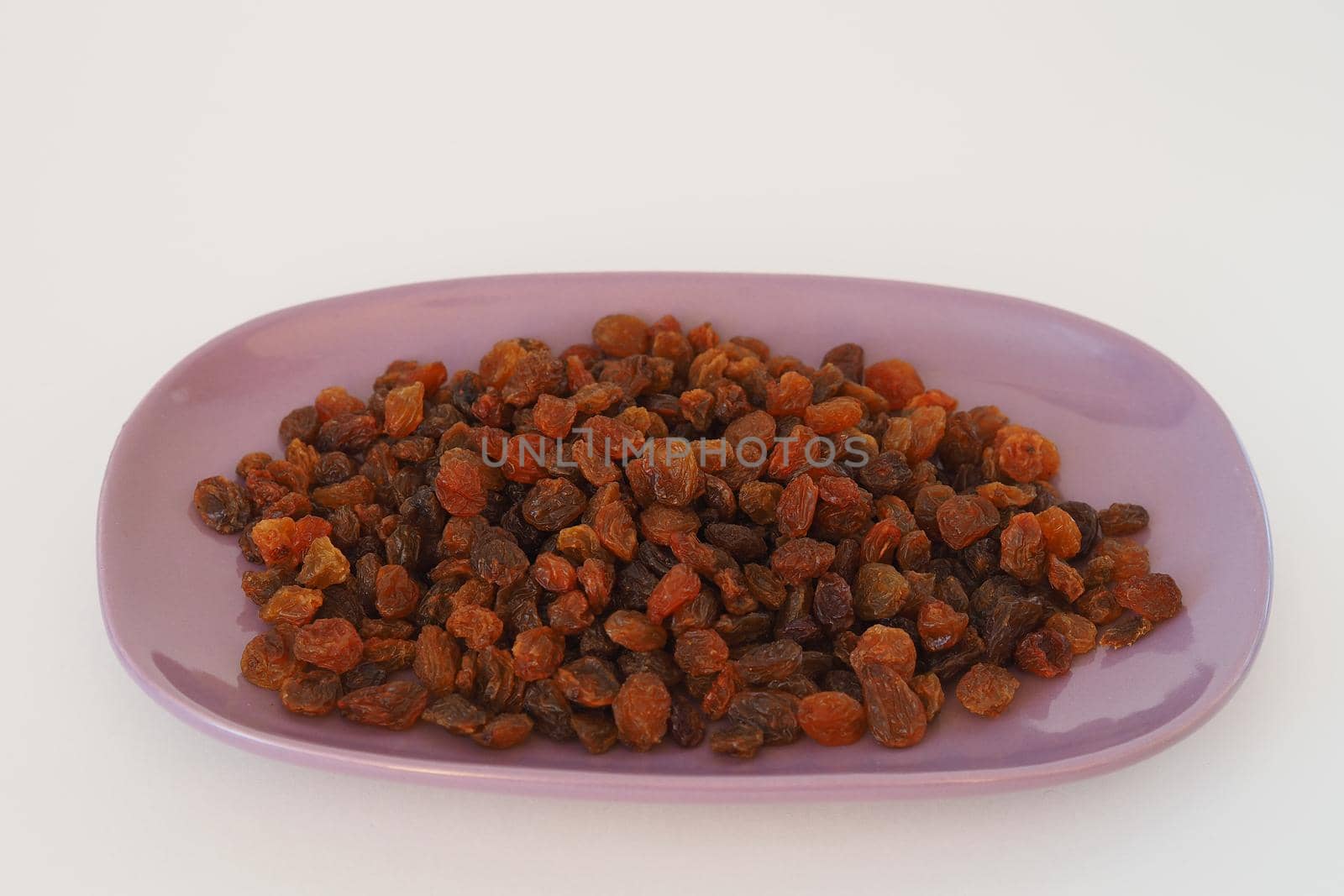 Dark raisins on a beautiful dish. Dried delicacy. White background.