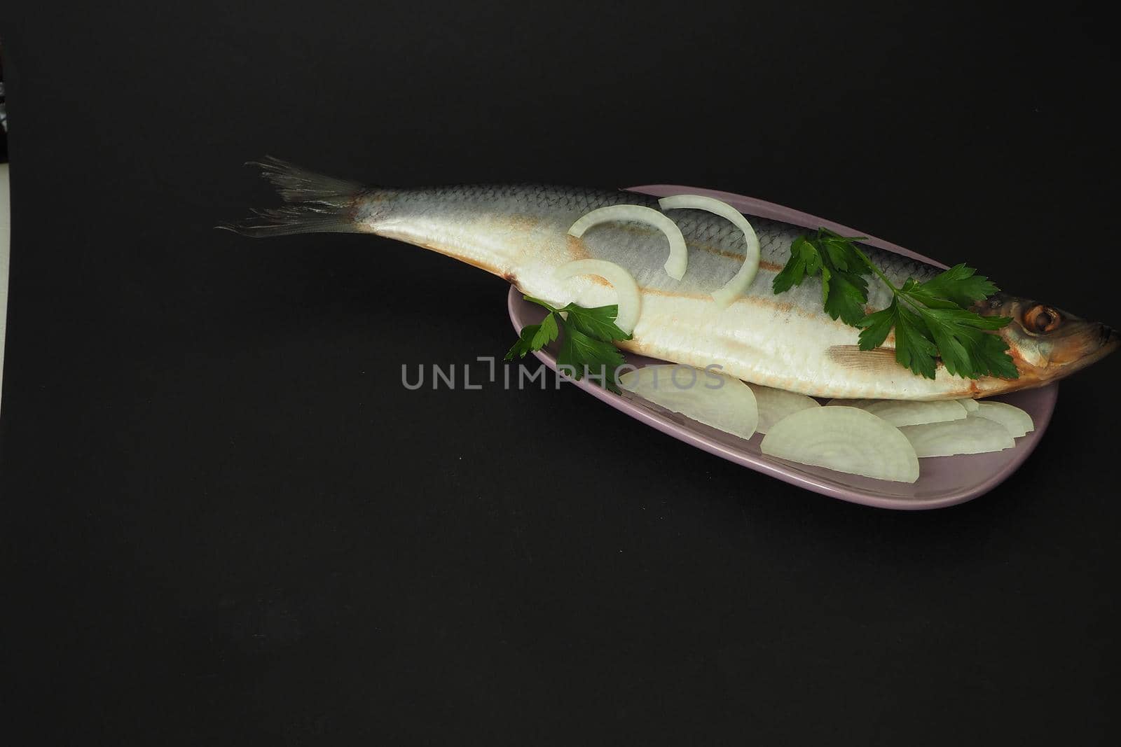 Herring whole, undivided with onion and parsley, close-up. Fish on a platter. Black background.