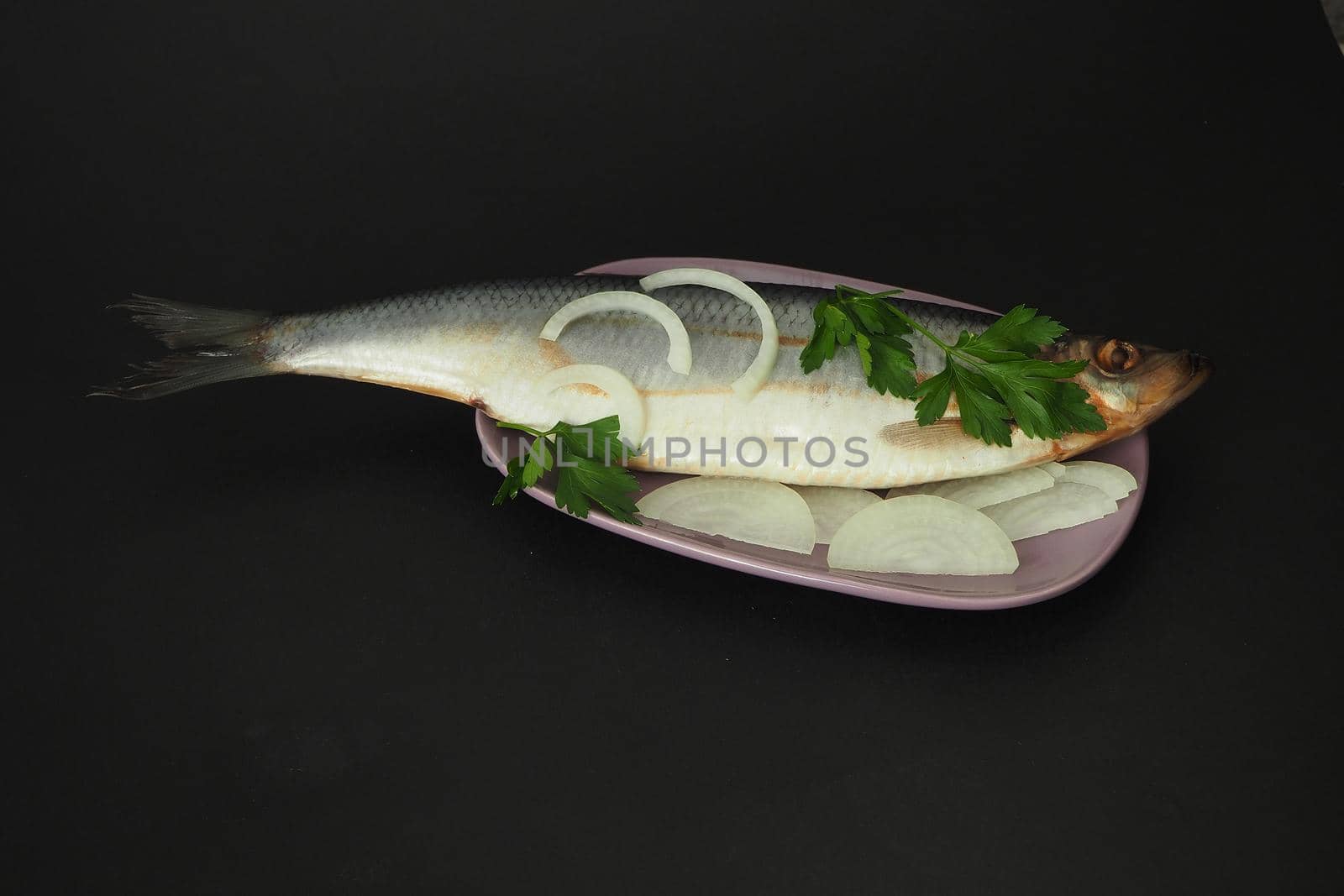 Herring whole, undivided with onion and parsley, close-up. Fish on a platter. Black background.