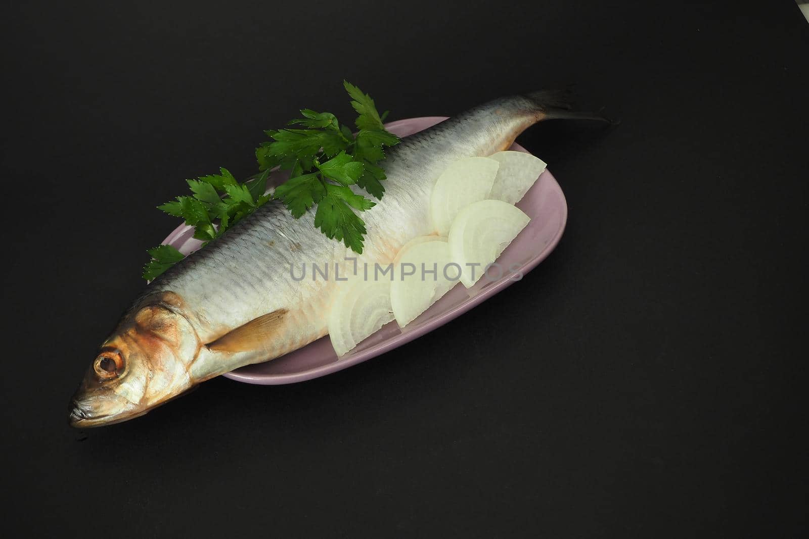 Herring whole, undivided with onion and parsley, close-up. Fish on a platter. Black background.