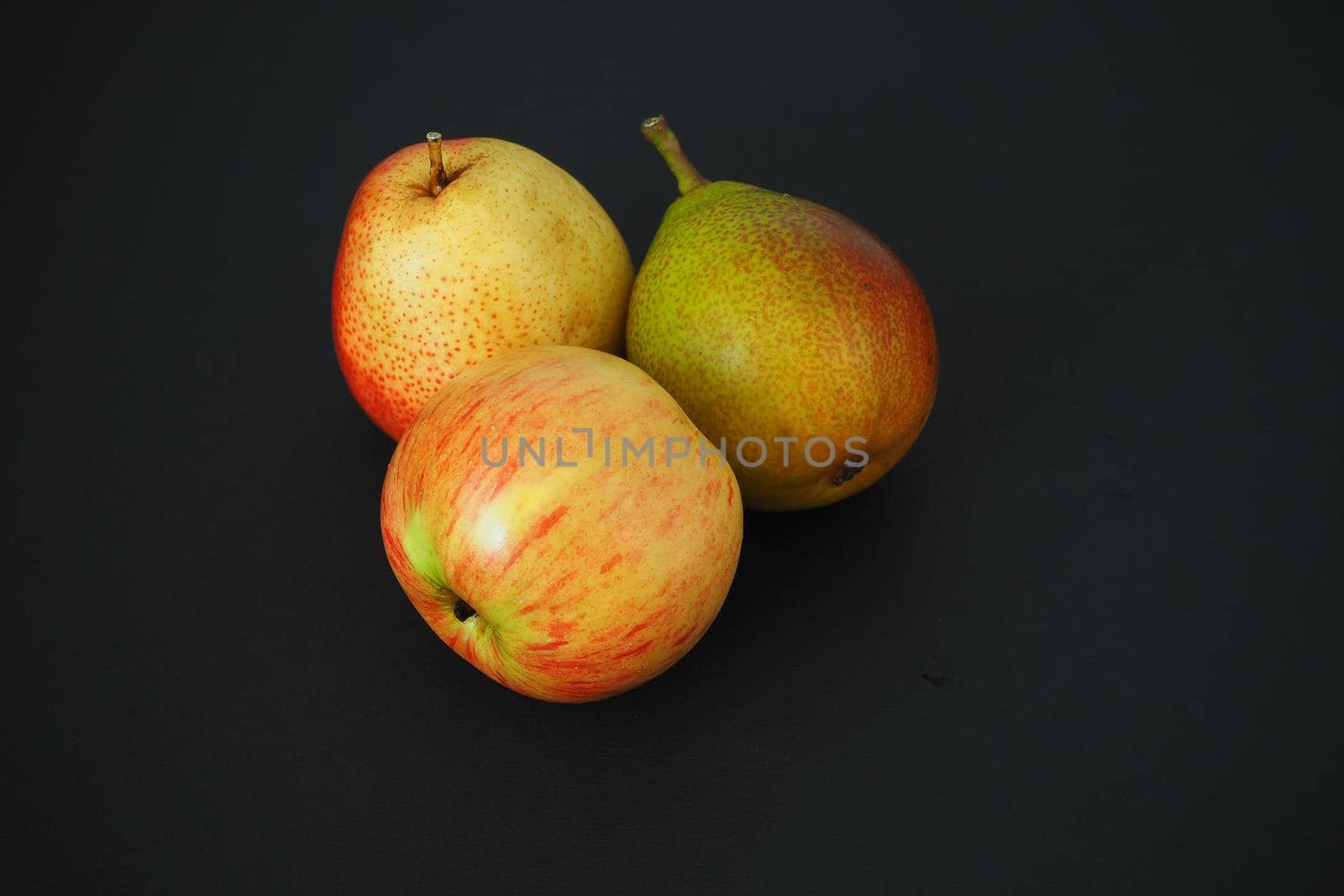 Two ripe pears and one beautiful apple. Close-up, black background, horizontal image.