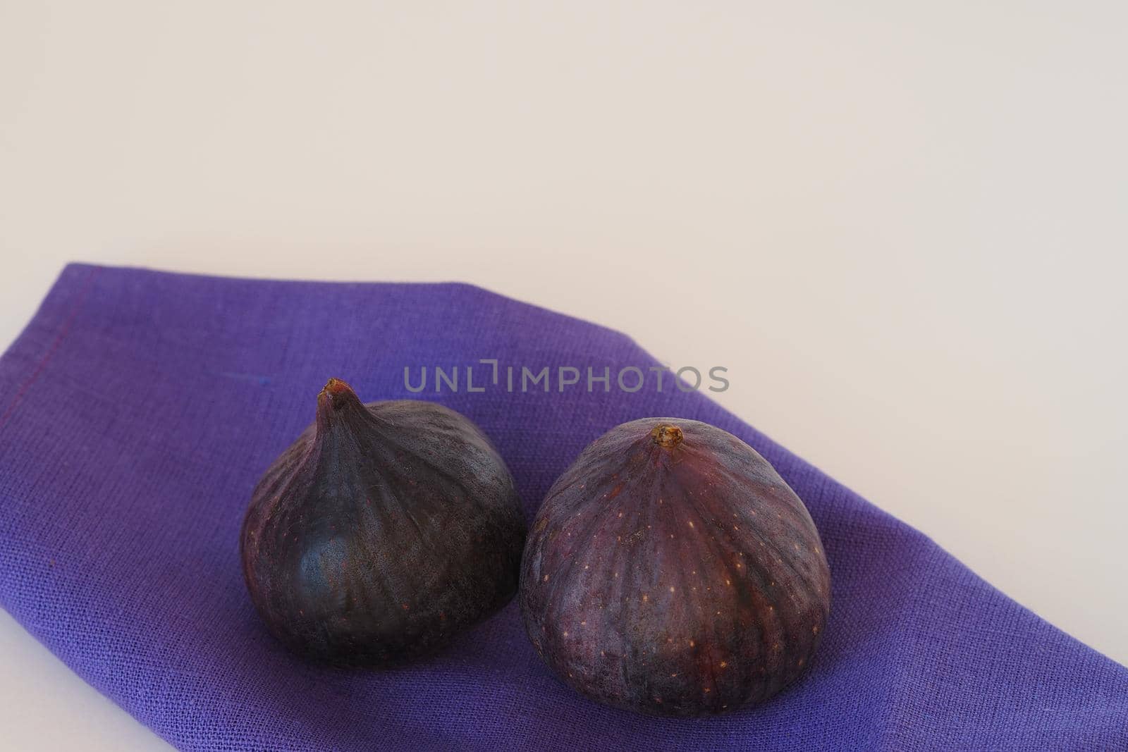 Two purple figs on a blue napkin. White background, close-up. by Olga26