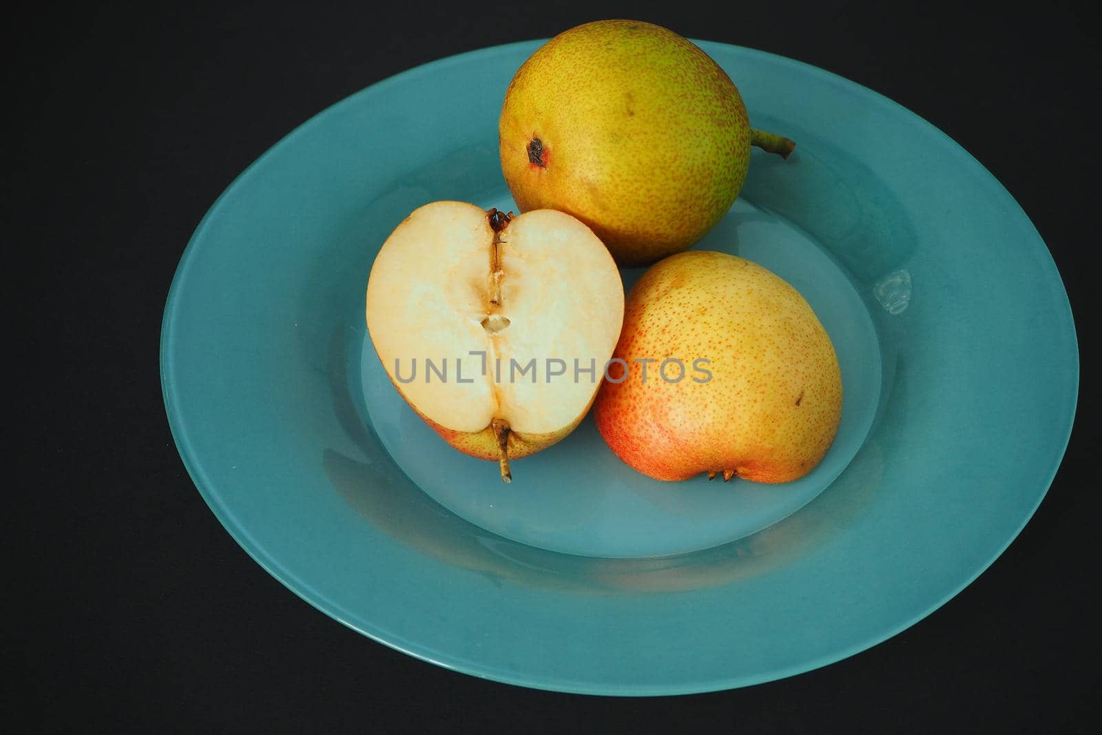 Ripe fruit. Pear on a platter cut into pieces. Black background, horizontal image.