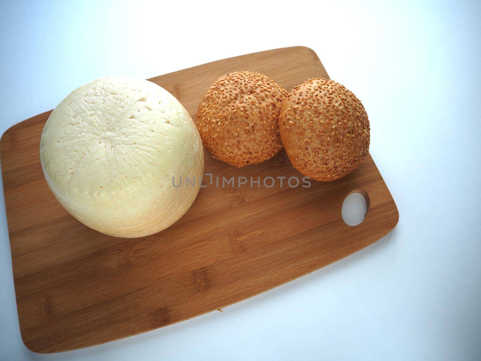 Round head of cheese with a sesame bun on a wooden tray close-up, view from above, white background.