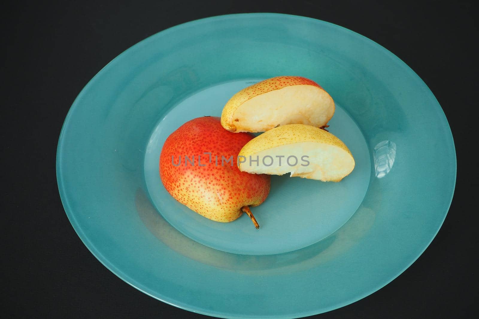 Ripe fruit. Pear on a platter cut into pieces. Black background, horizontal image.