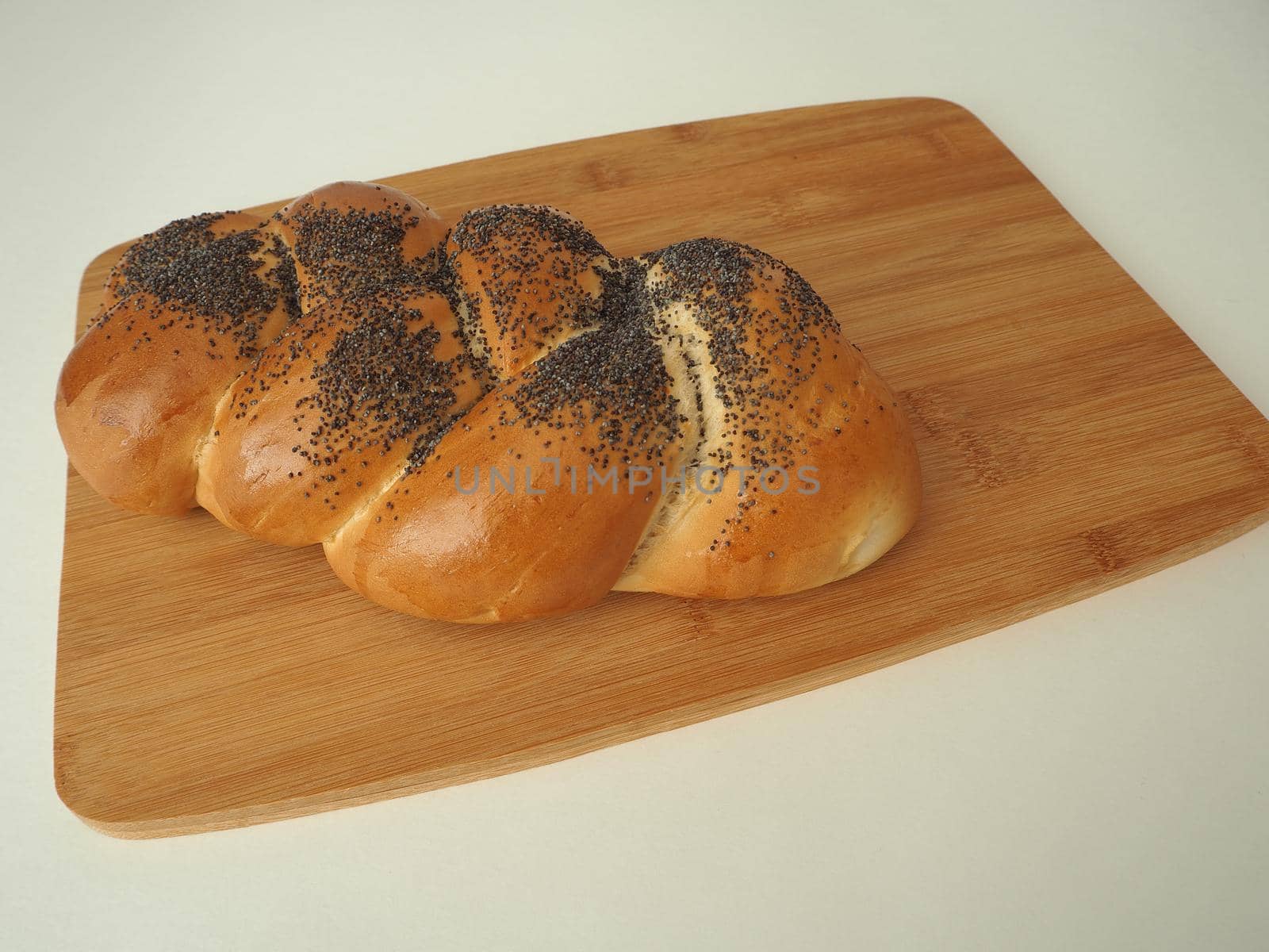 Fresh bread on a wooden tray. A cosy bun with a close-up poppy. White background.