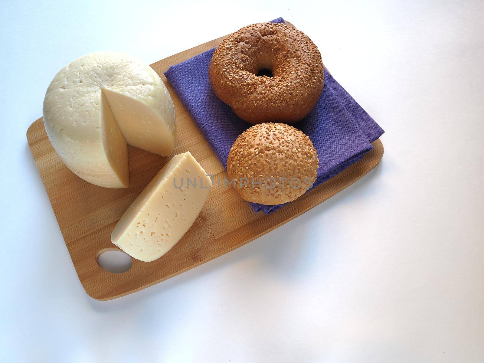 The cheese is a round head cut with bread, baguette, sesame bun. glass of milk on a wooden tray, a piece of cheese. 