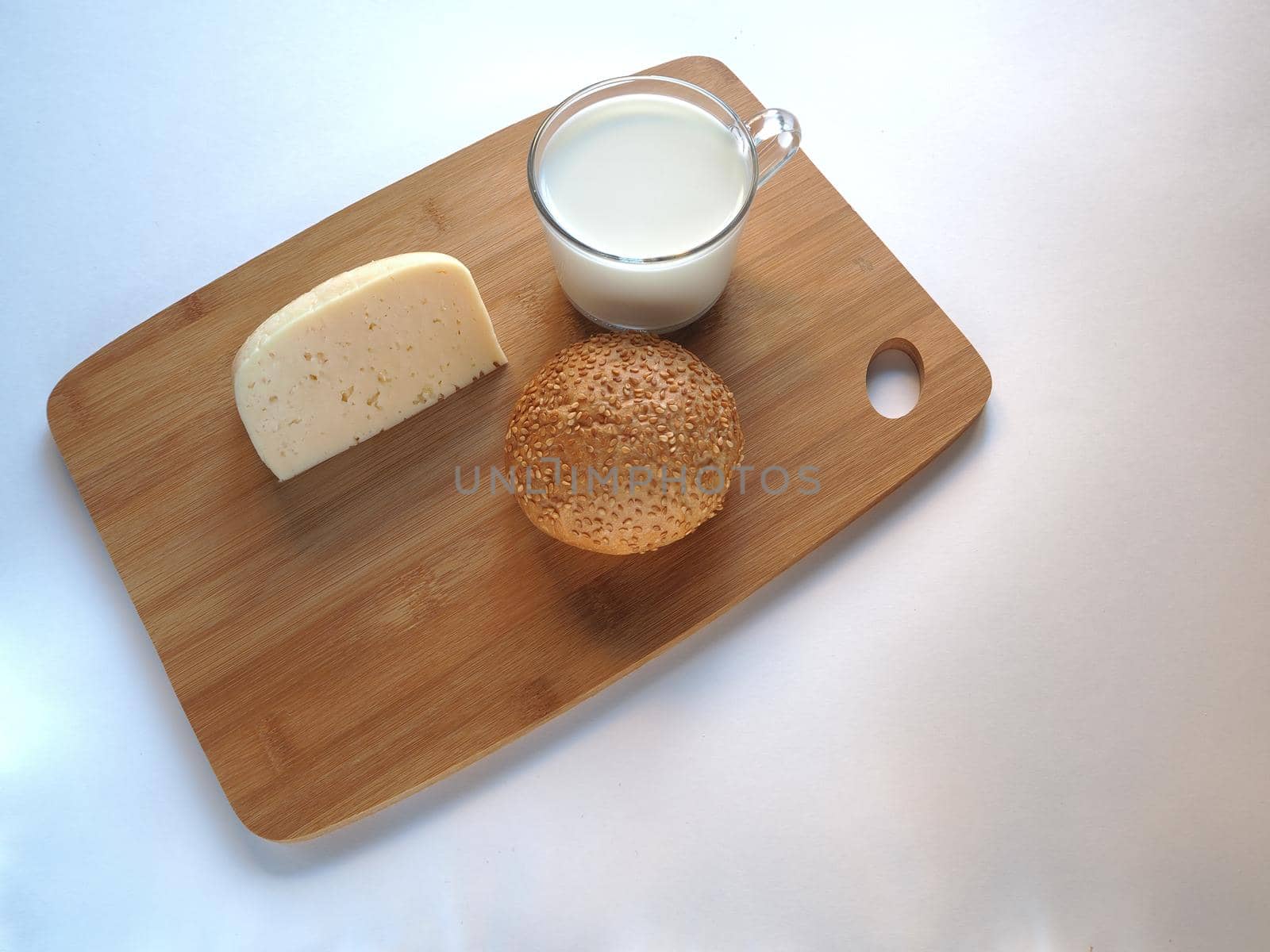 A piece of cheese with a sesame bun and a glass of milk on a wooden tray. by Olga26