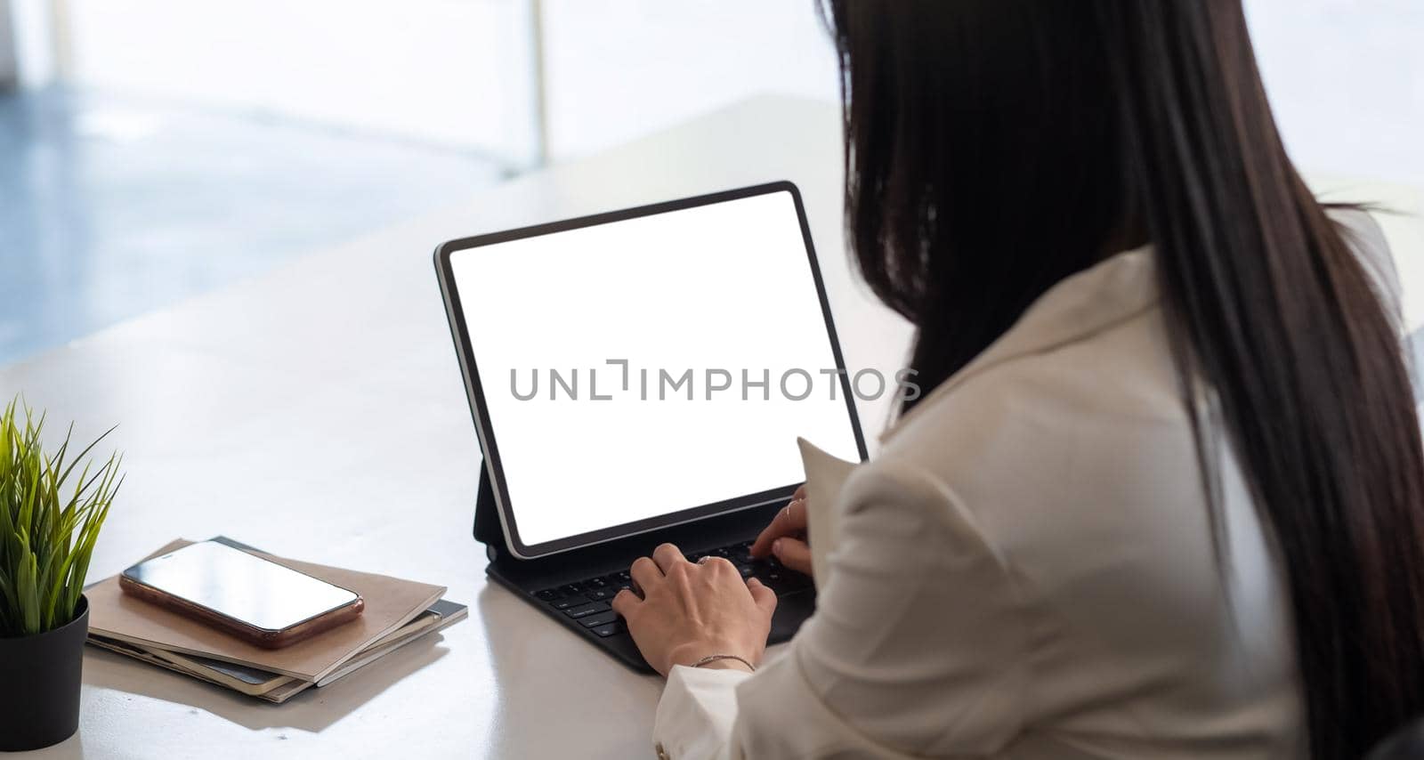 Cropped shot of business woman hand while typing on computer tablet with blank screen and sitting next to her colleague by nateemee