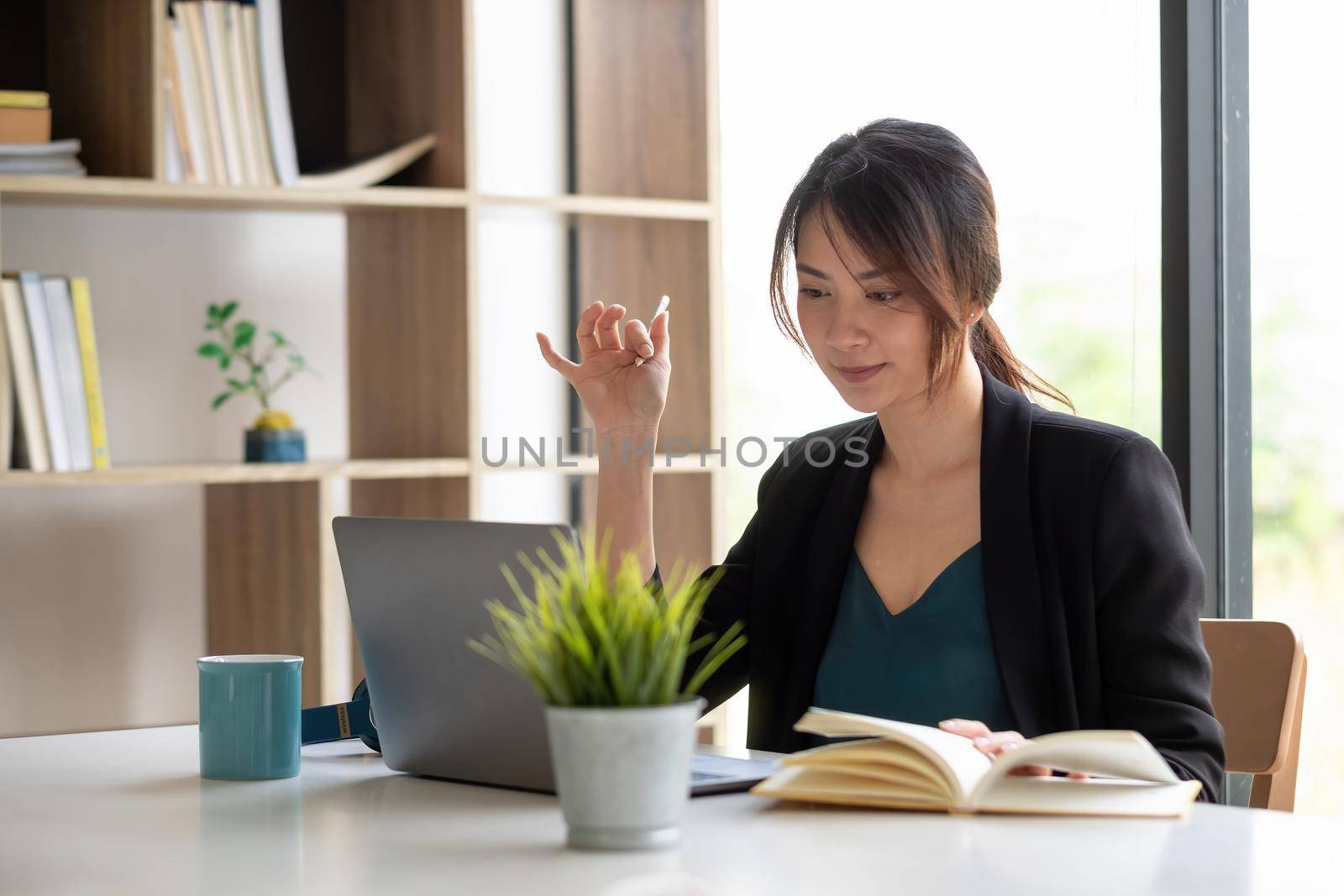 Asian businesswoman talking to colleague team in video call conference writing note on book with smile face by nateemee
