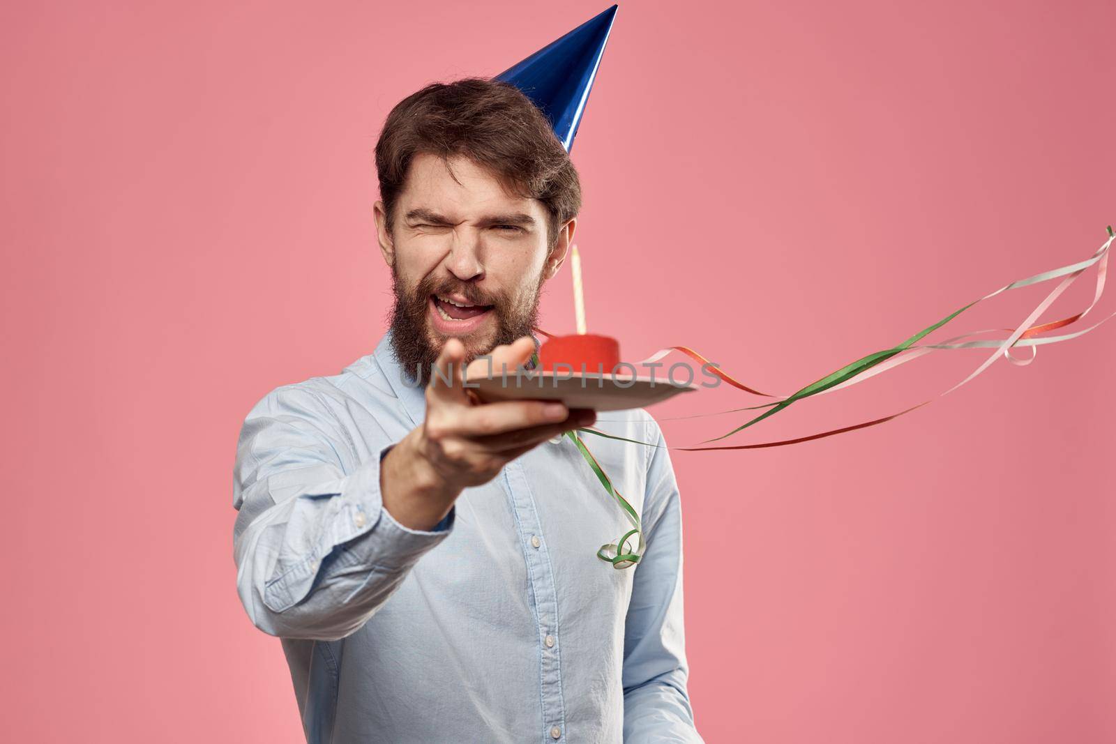 Bearded man with cake tongue on a pink background cropped view and a blue cap on his head. High quality photo