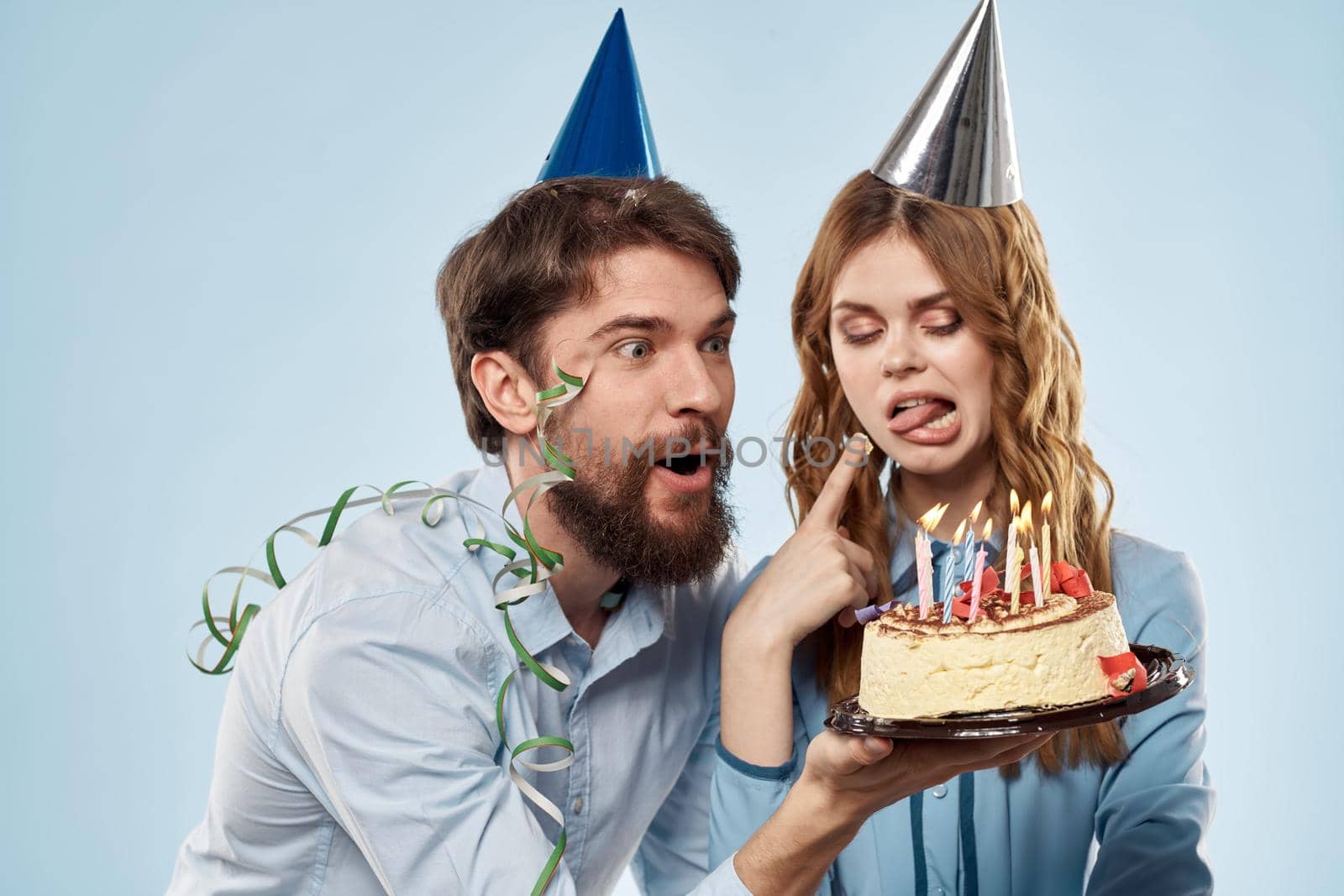 man and woman celebrate birthday with cake and in hats on blue background. High quality photo