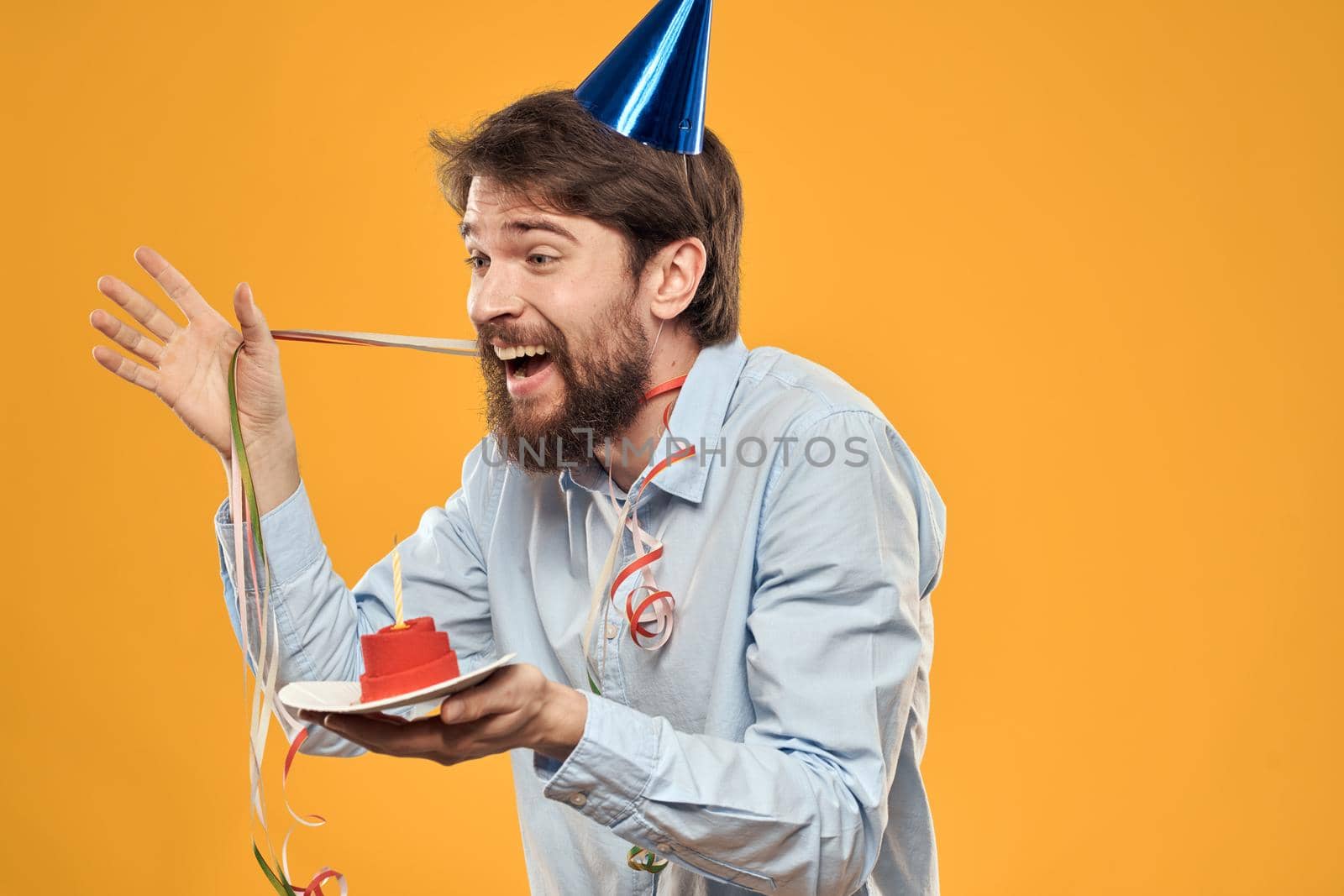 Cheerful man with a cake on a yellow background birthday holidays cap on his head. High quality photo