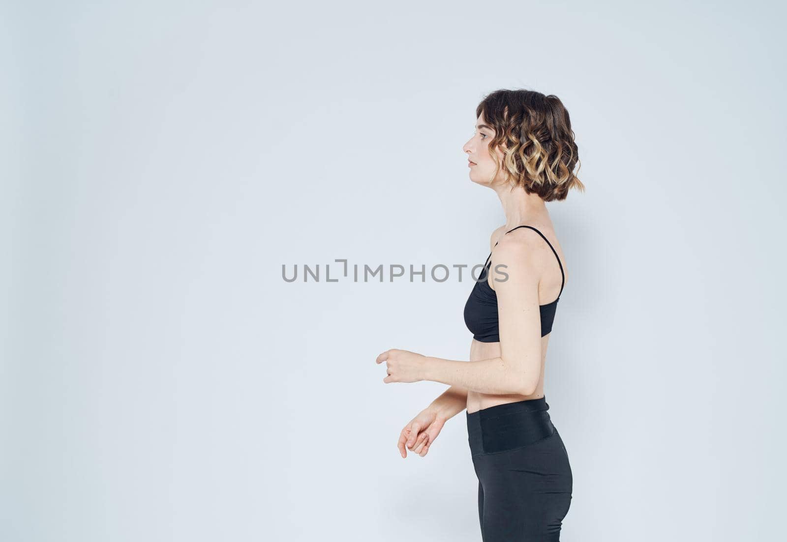 A sportive woman is doing exercises on a light background gesturing with her hands. High quality photo