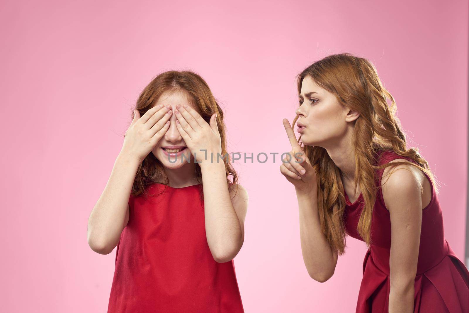 Cheerful mom and daughter wearing red dresses are standing next to joy family on pink background. High quality photo