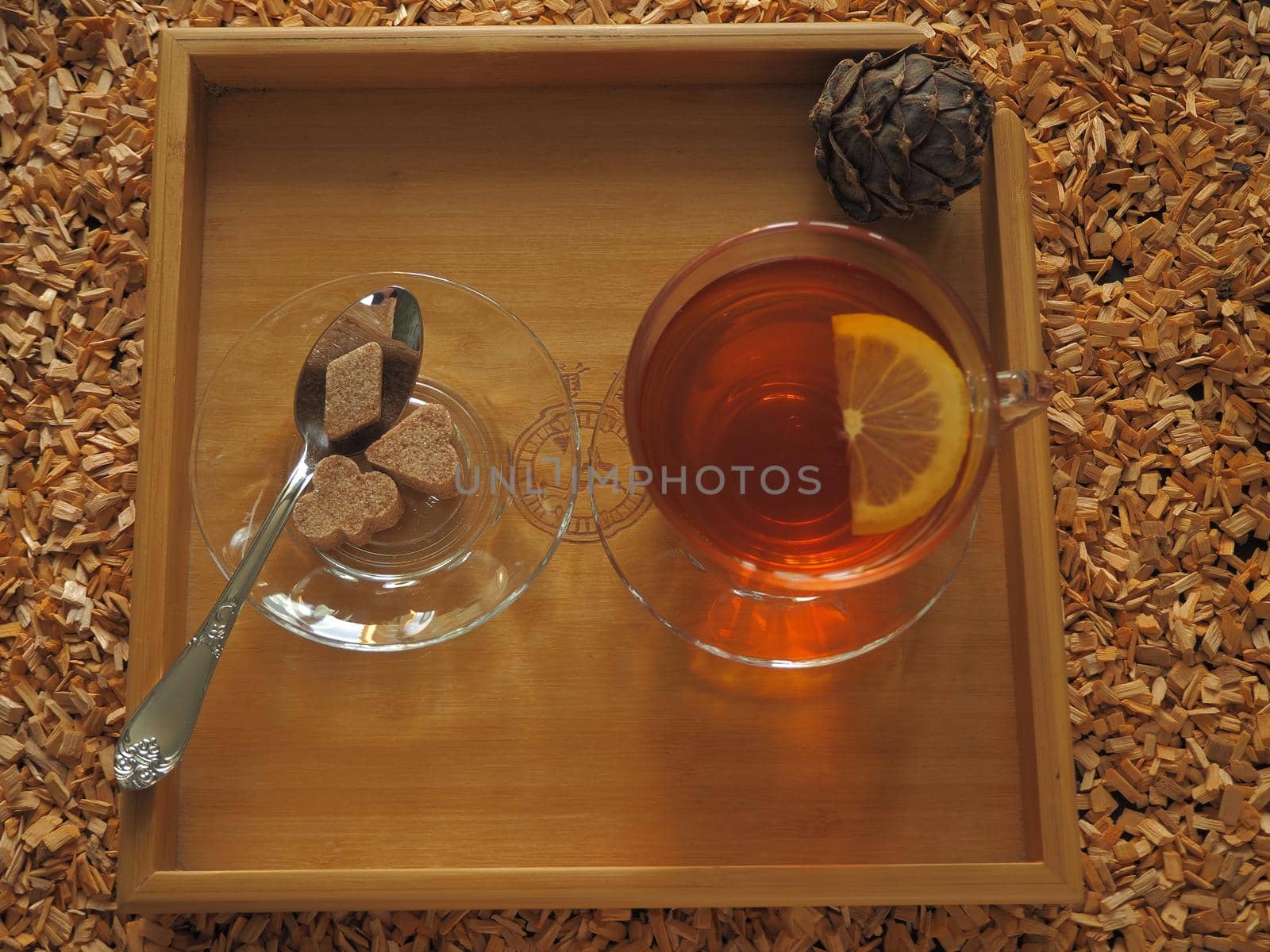 Black tea with lemon in a transparent cup on a wooden tray.