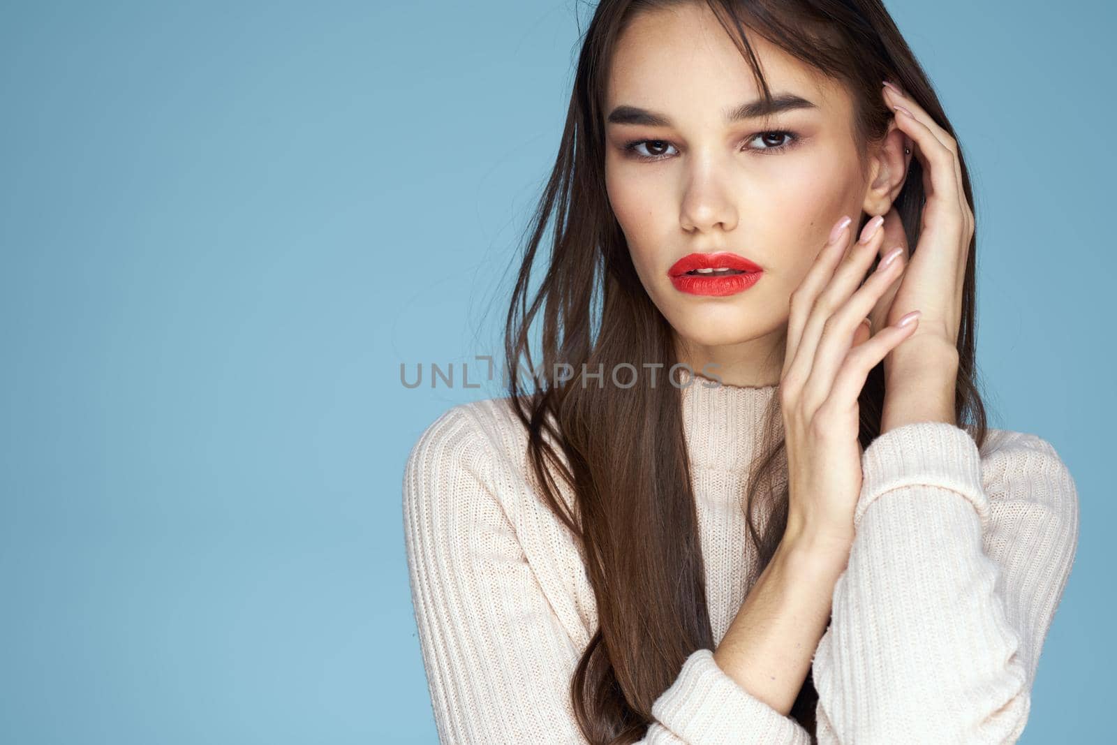 Brunette in a white sweater red lips charm long hair blue background. High quality photo