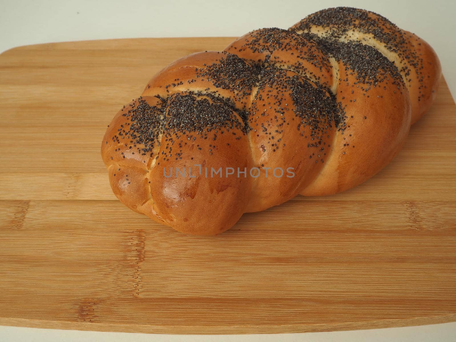 Fresh bread on a wooden tray. A cosy bun with a close-up poppy. White background.