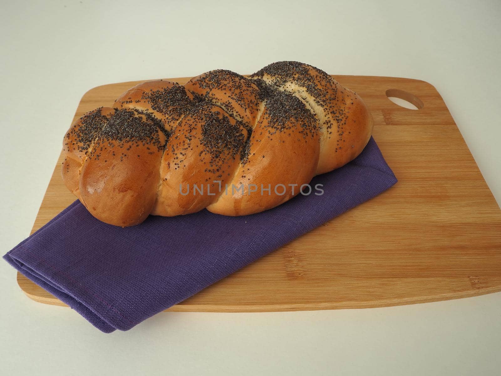 A loaf of bread, a bun pigtail with a poppy close-up on a wooden Board. Baking with pastry poppy. 