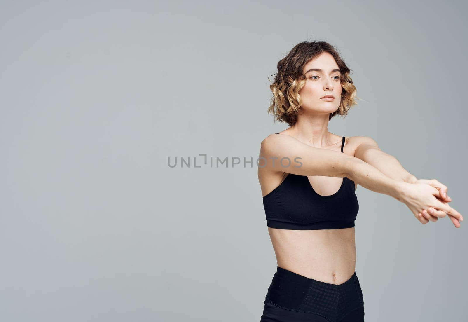 A woman in dark sportswear on a gray background gestures with her hands by SHOTPRIME