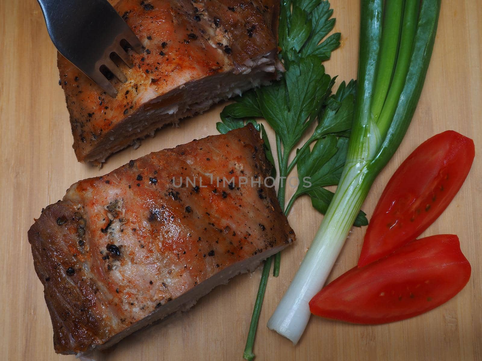 Baked meat on a platter with tomato and herbs. Pork carbonate.