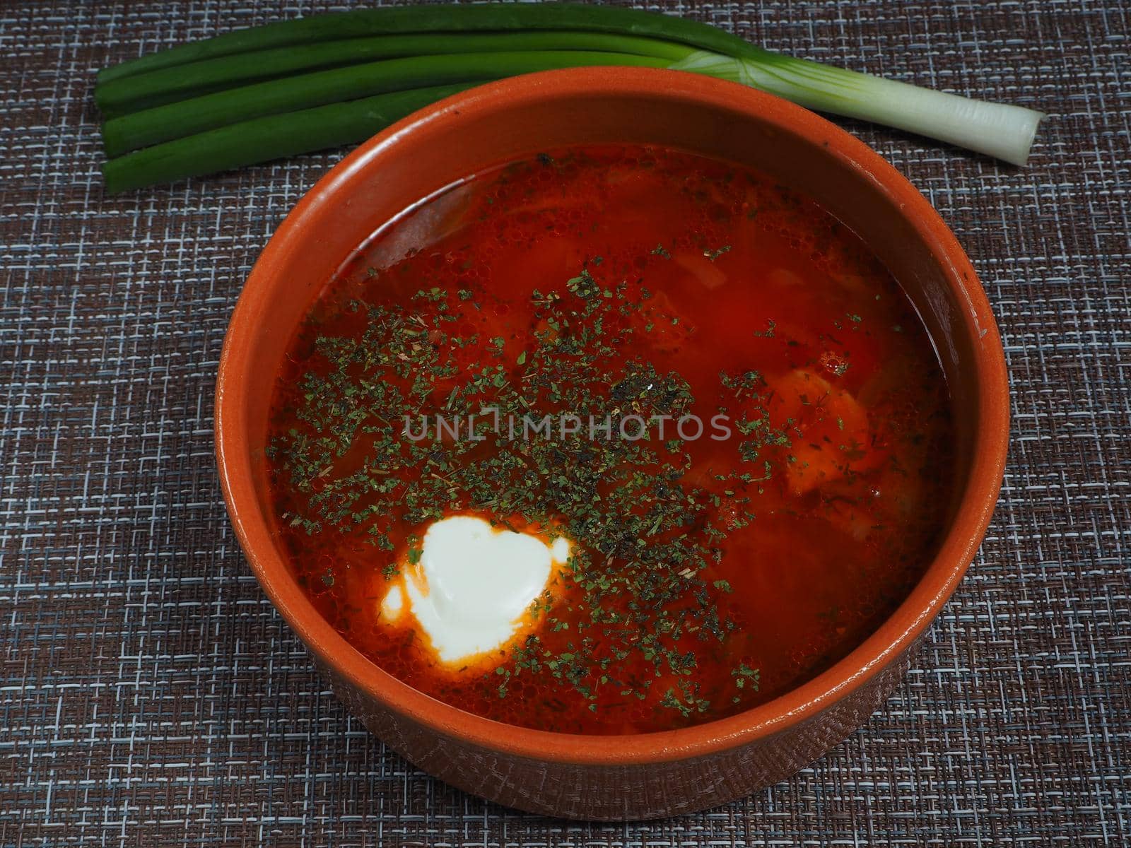 Red borscht in a deep plate with green onions. Close-up. A quality image.