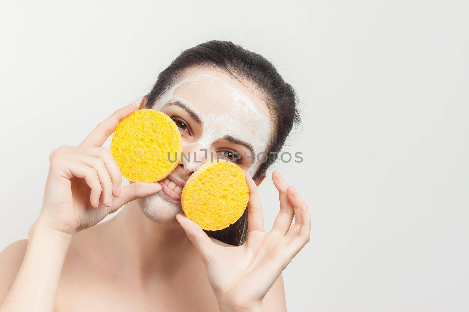 brunette with bare shoulders gathered hair facial mask sponge. High quality photo
