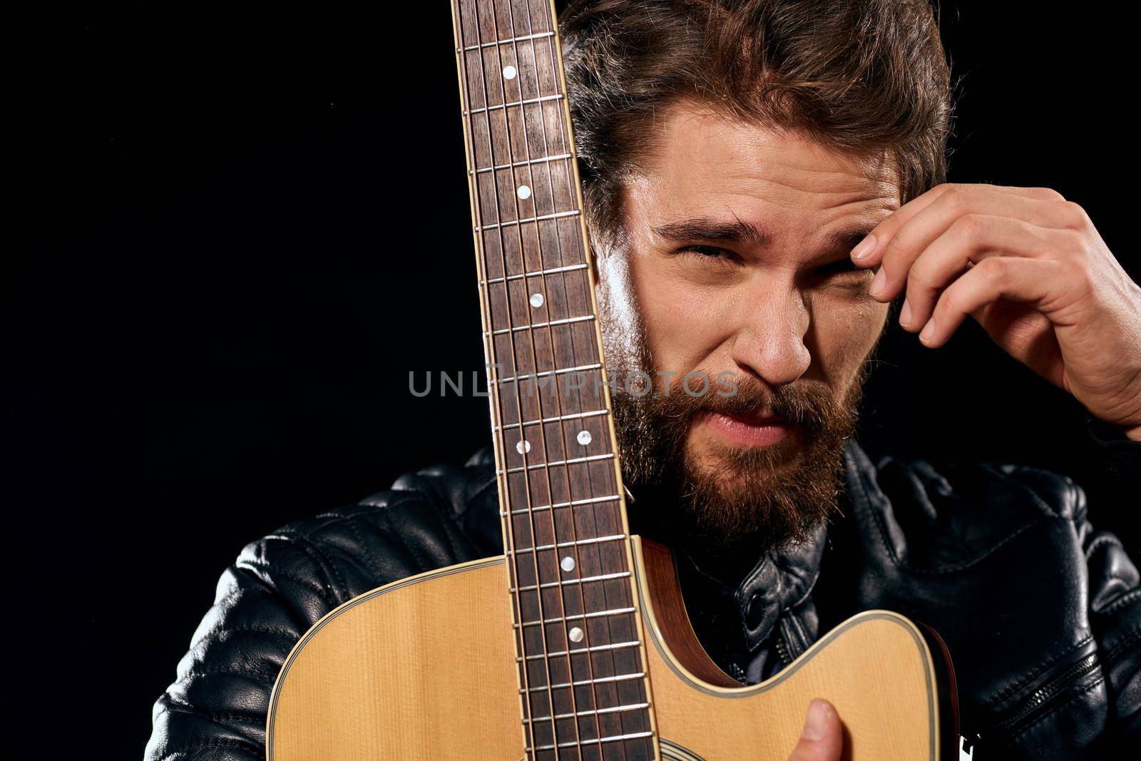 A man with a guitar in his hands leather jacket music performance rock star modern style dark background. High quality photo