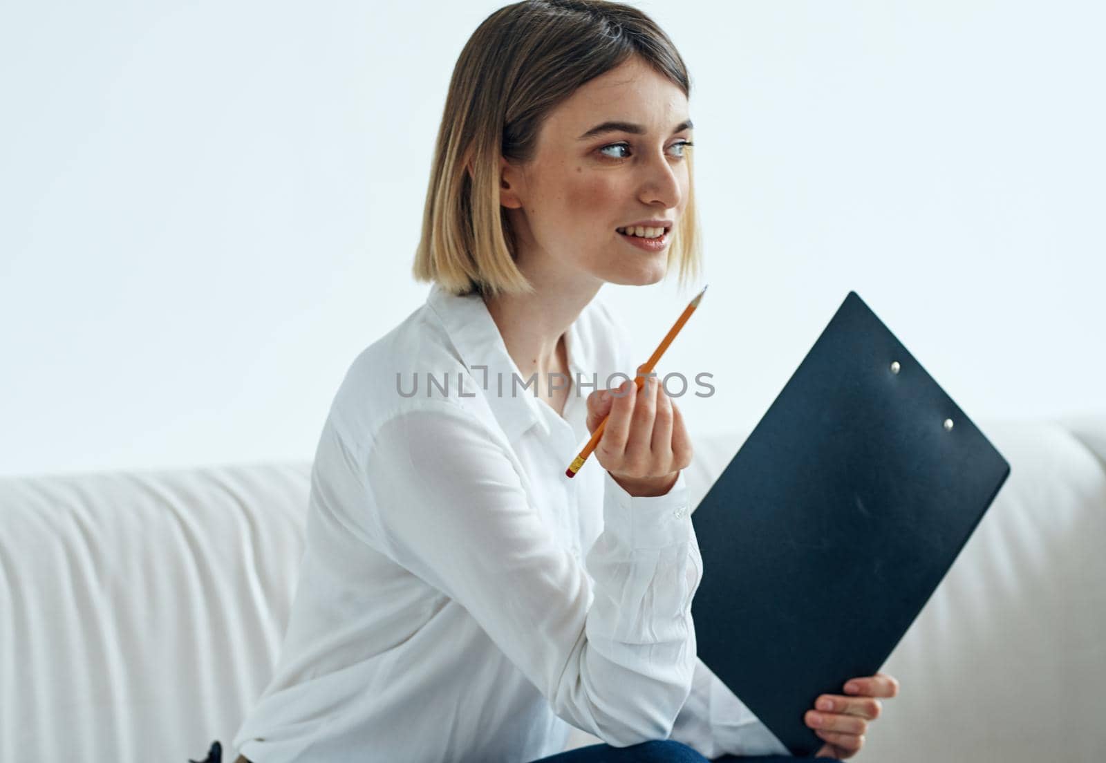 A woman sits on a sofa In a bright room in a shirt and papers . High quality photo