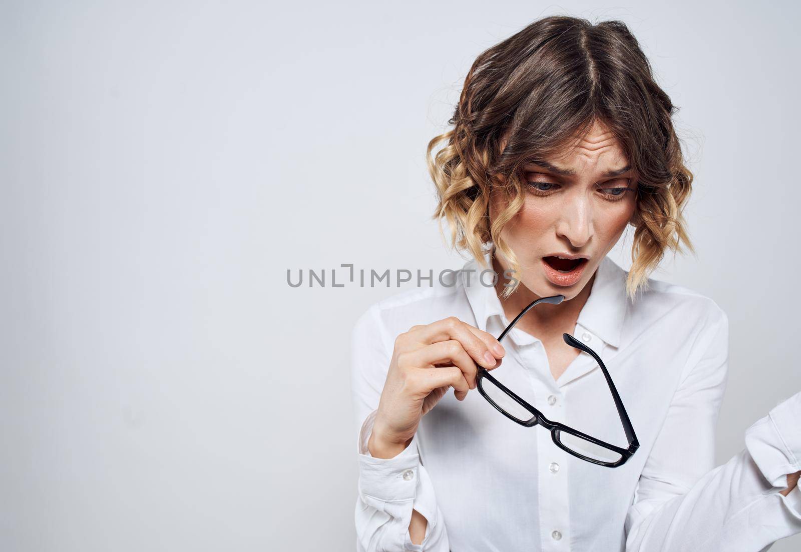 A beautiful woman in a white shirt holds glasses in her hands on a light background. High quality photo