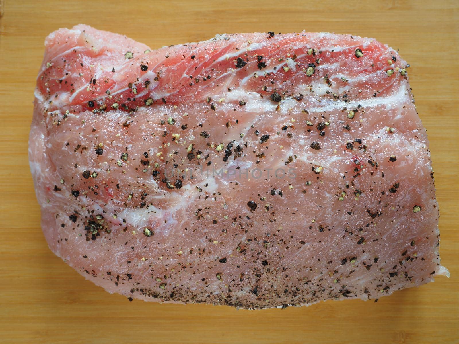 Fresh raw meat. Pork for baking with pepper and spices. A wooden background. Close-up.