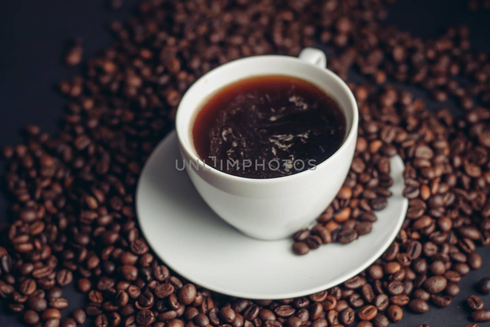 coffee beans and a cup on a white saucer dark background drink. High quality photo