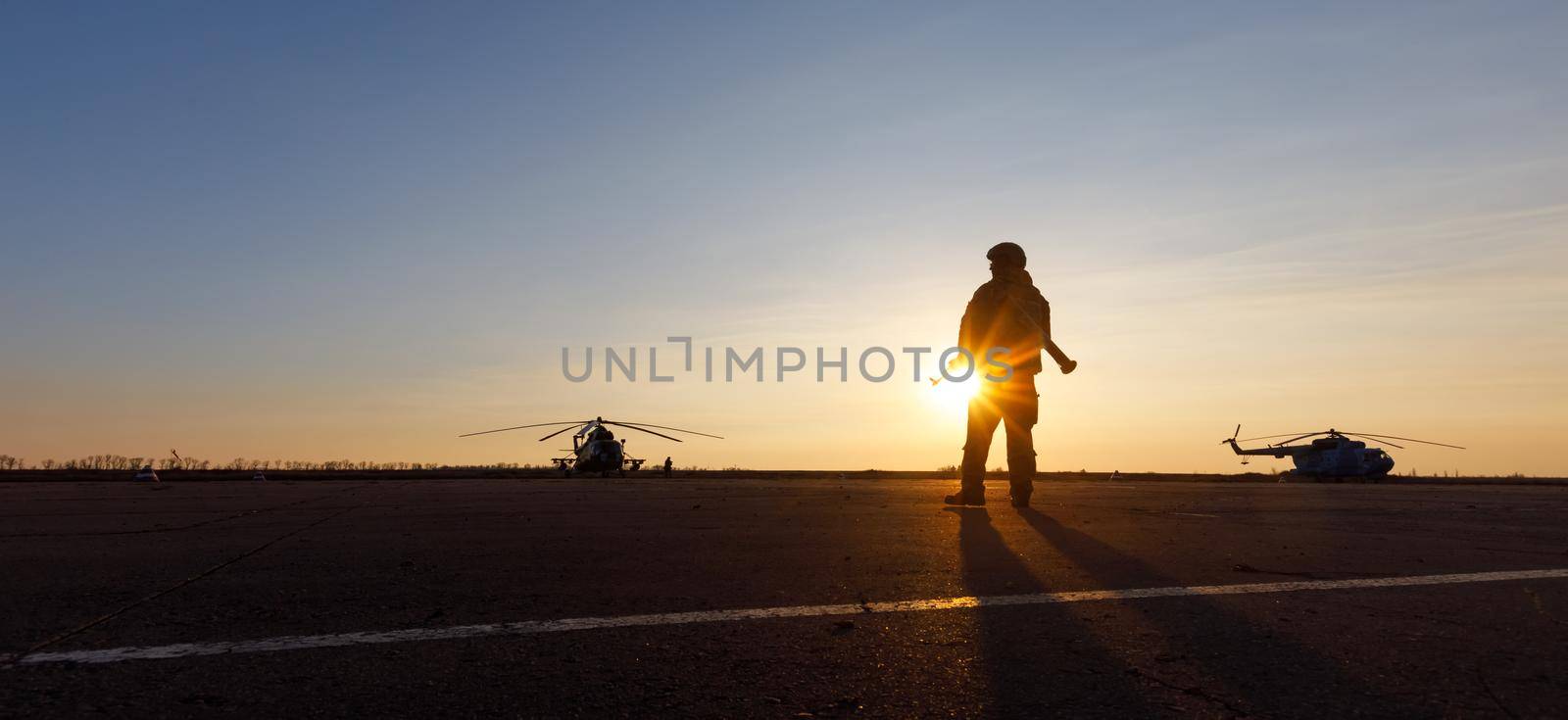 MARIUPOL, UKRAINE - Nov. 16, 2017: Silhouette of a military man with a machine gun in a combat post against the helicopters and sunset sky during festivities on occasion of the Day of Naval Infantry