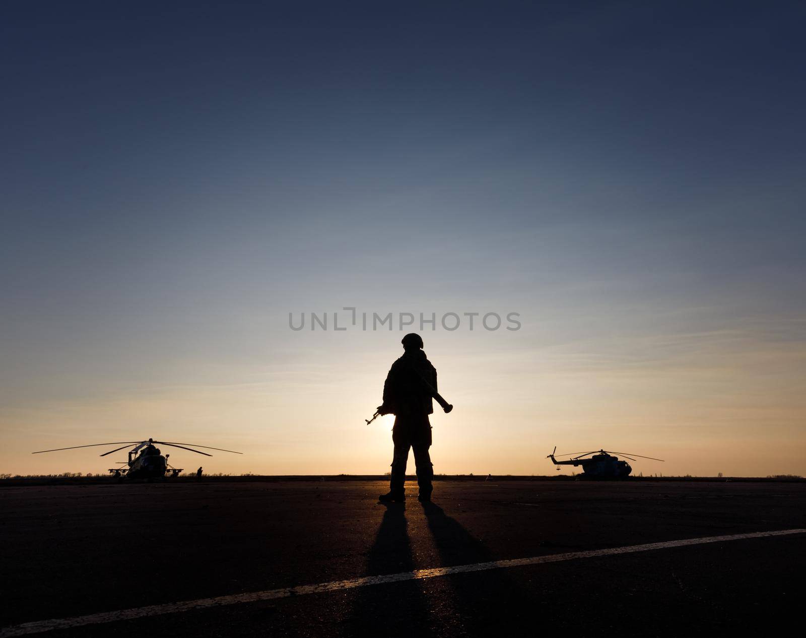 MARIUPOL, UKRAINE - Nov. 16, 2017: Silhouette of a military man with a machine gun in a combat post against the helicopters and sunset sky during festivities on occasion of the Day of Naval Infantry