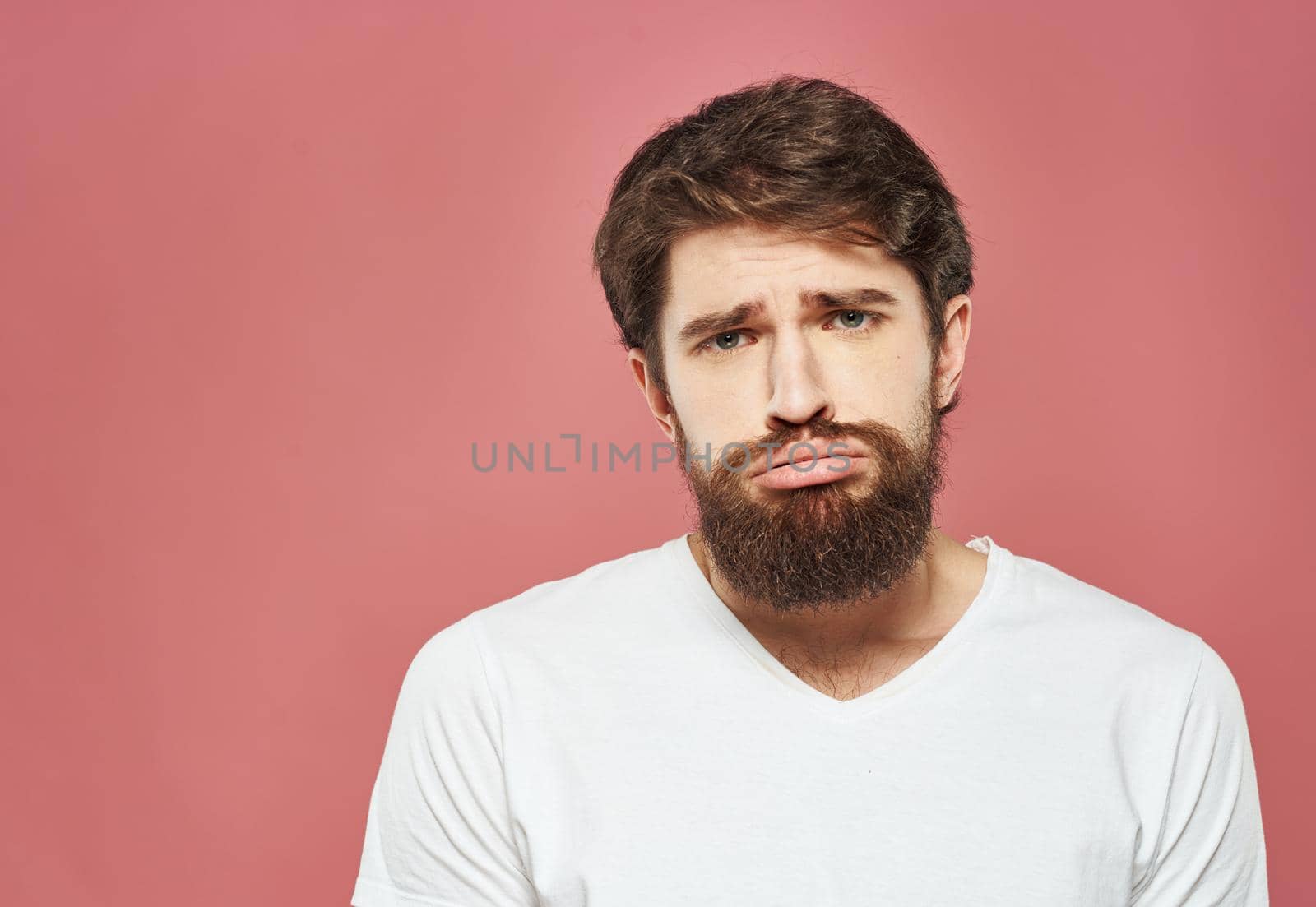 Sad man on pink background cropped view of white t-shirt and bushy beard. High quality photo